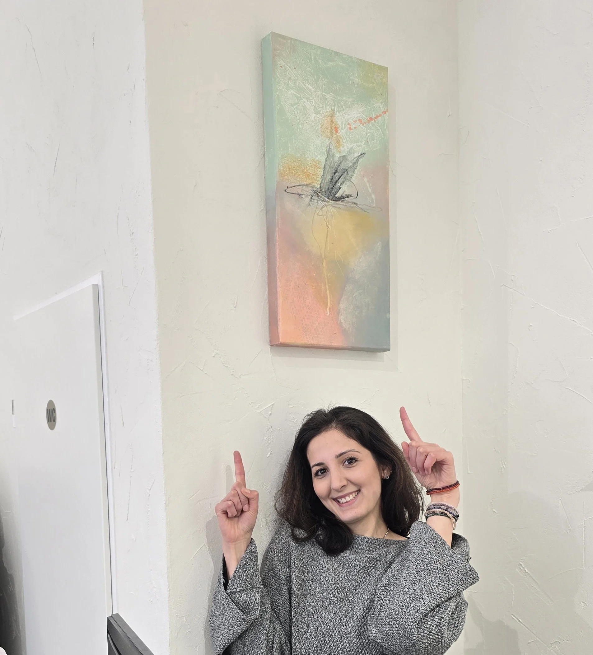 Die Inhaberin des Salon ARose in Ulm, Gülnur Ata, zeigt nach oben auf eine abstrakte Leinwand von Stefanie Rau.