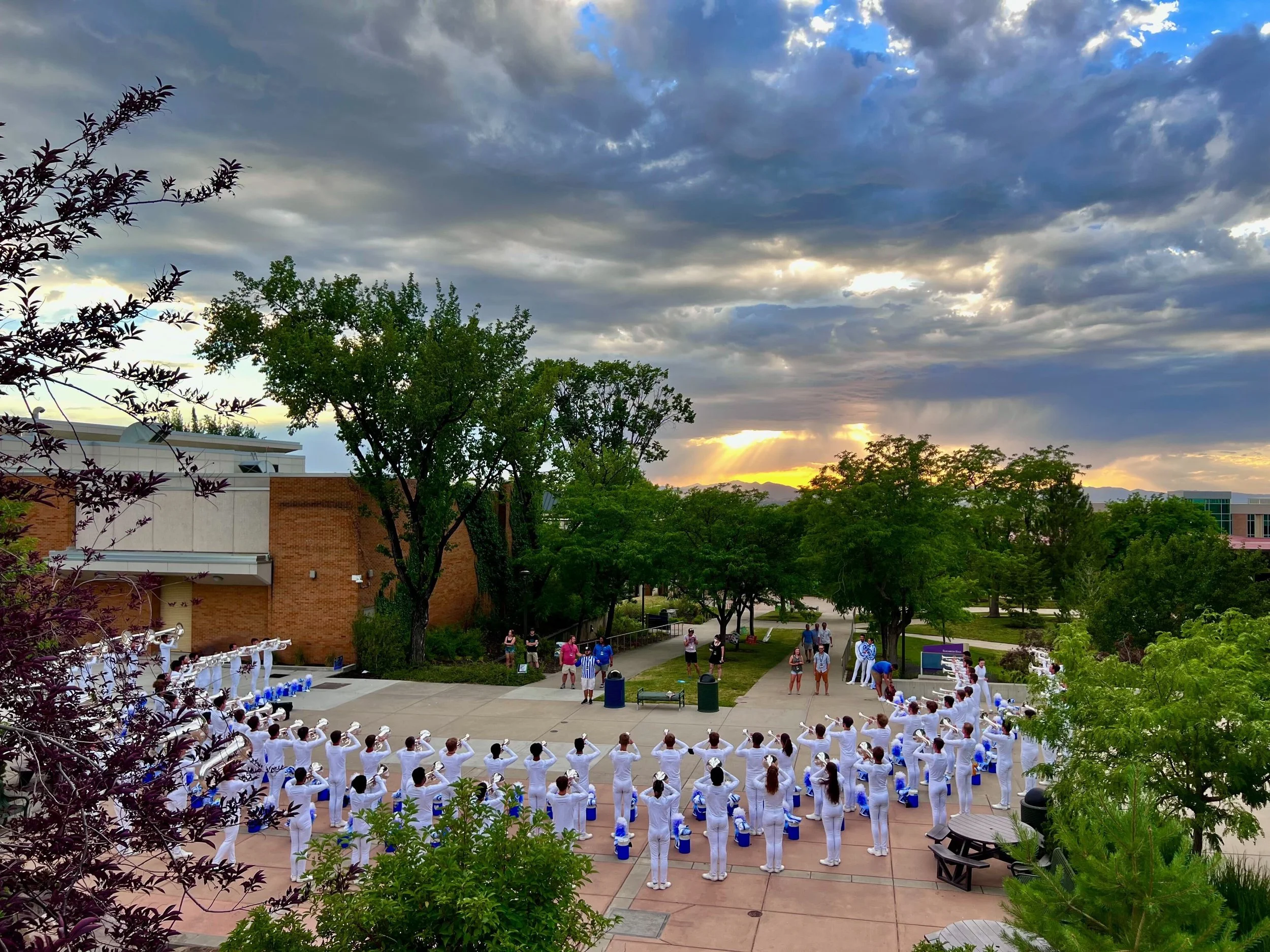 Students dressed in white uniforms standing in formation outdoors during sunset.