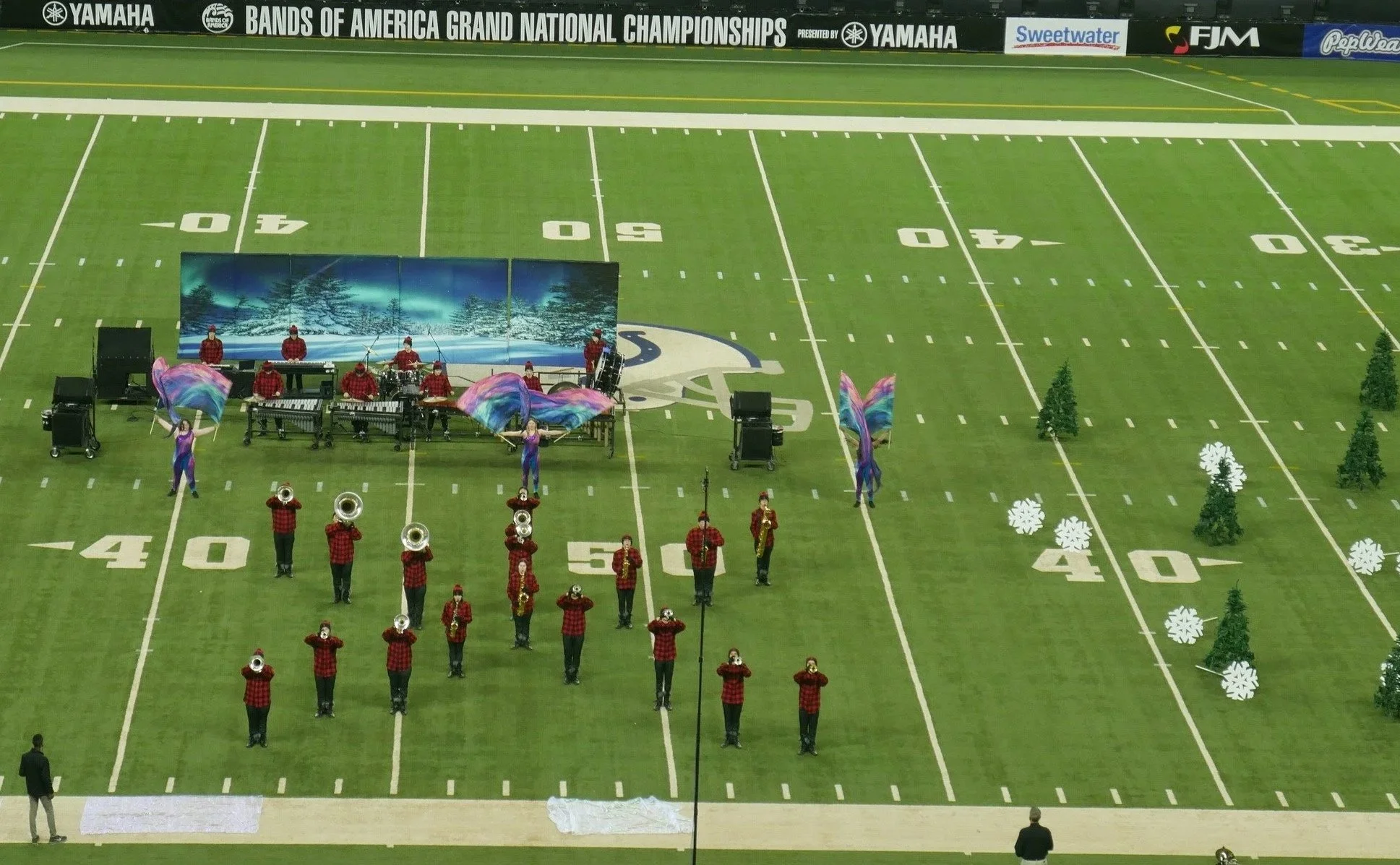 A marching band performing on a football field decorated with winter-themed props, including snowflakes and trees, during the Bands of America Grand National Championships.