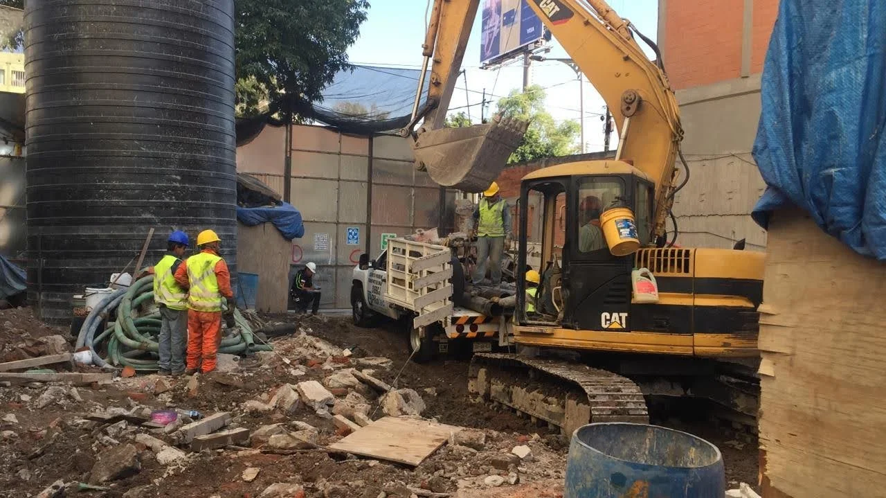 Construction site with workers and a yellow excavator clearing debris and digging.