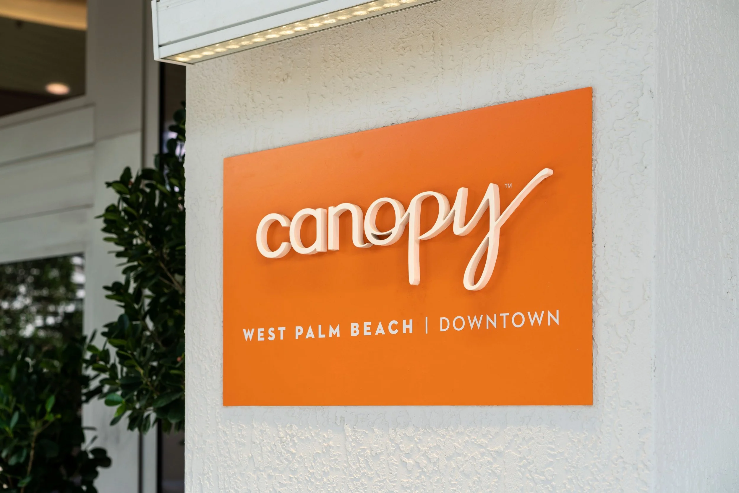 Orange sign on textured white wall reading "Canopy" with the words "West Palm Beach | Downtown" underneath.