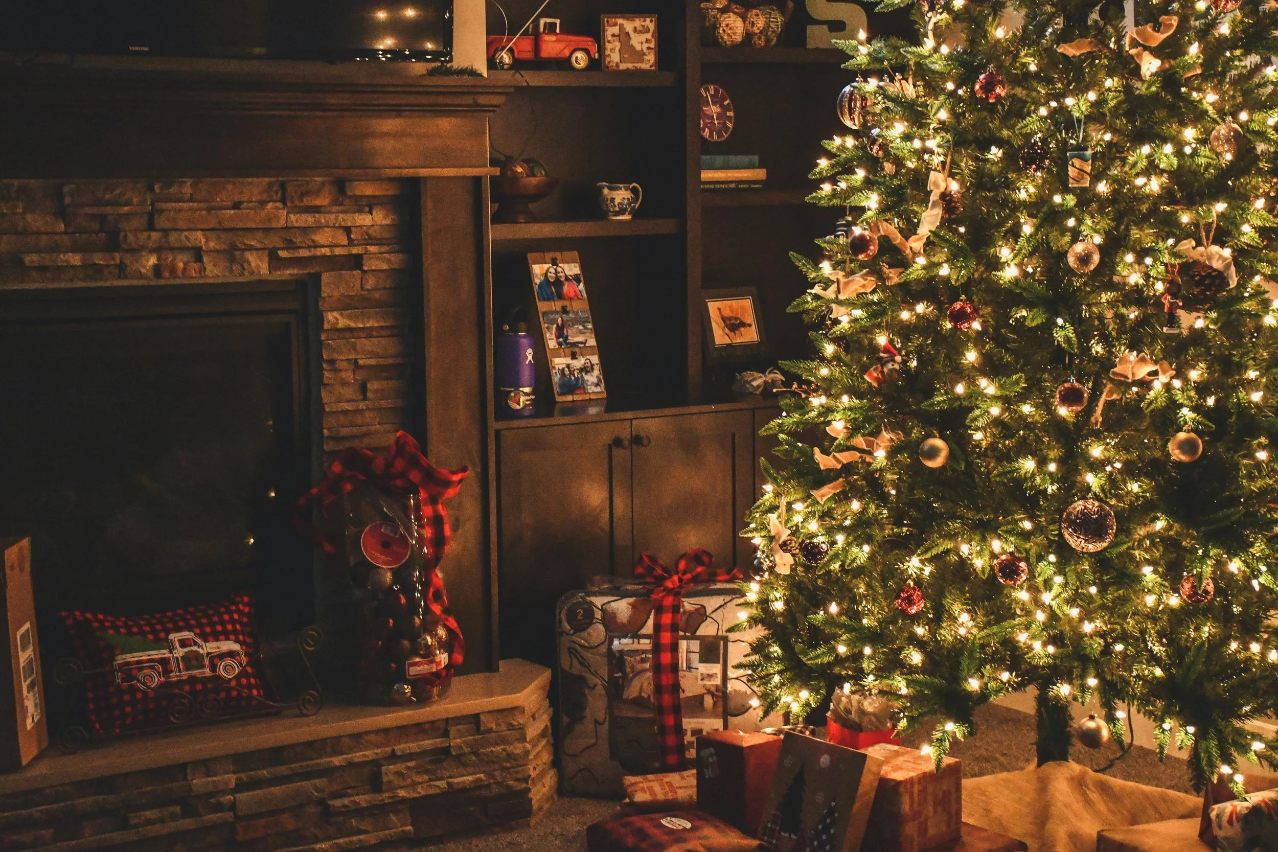 A decorated Christmas tree with lights and ornaments near a fireplace with stockings and wrapped gifts underneath, in a cozy living room.
