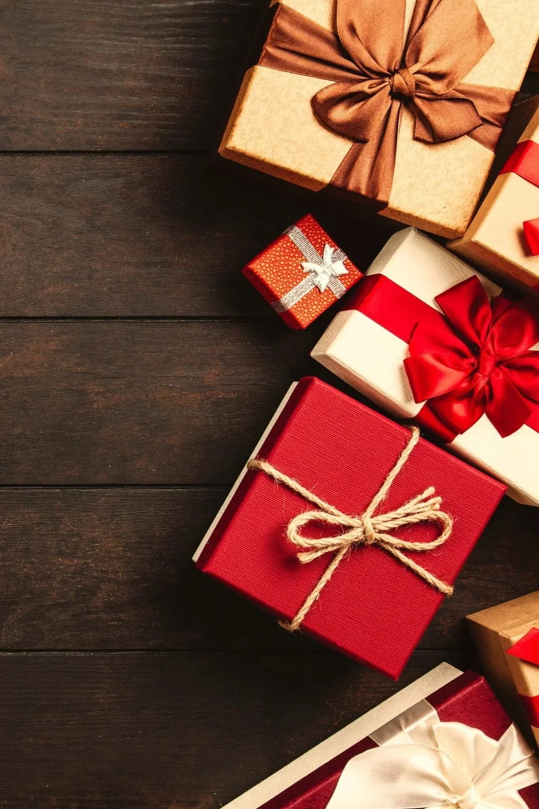 Various wrapped Christmas gifts on a dark wooden surface, decorated with ribbons and bows.