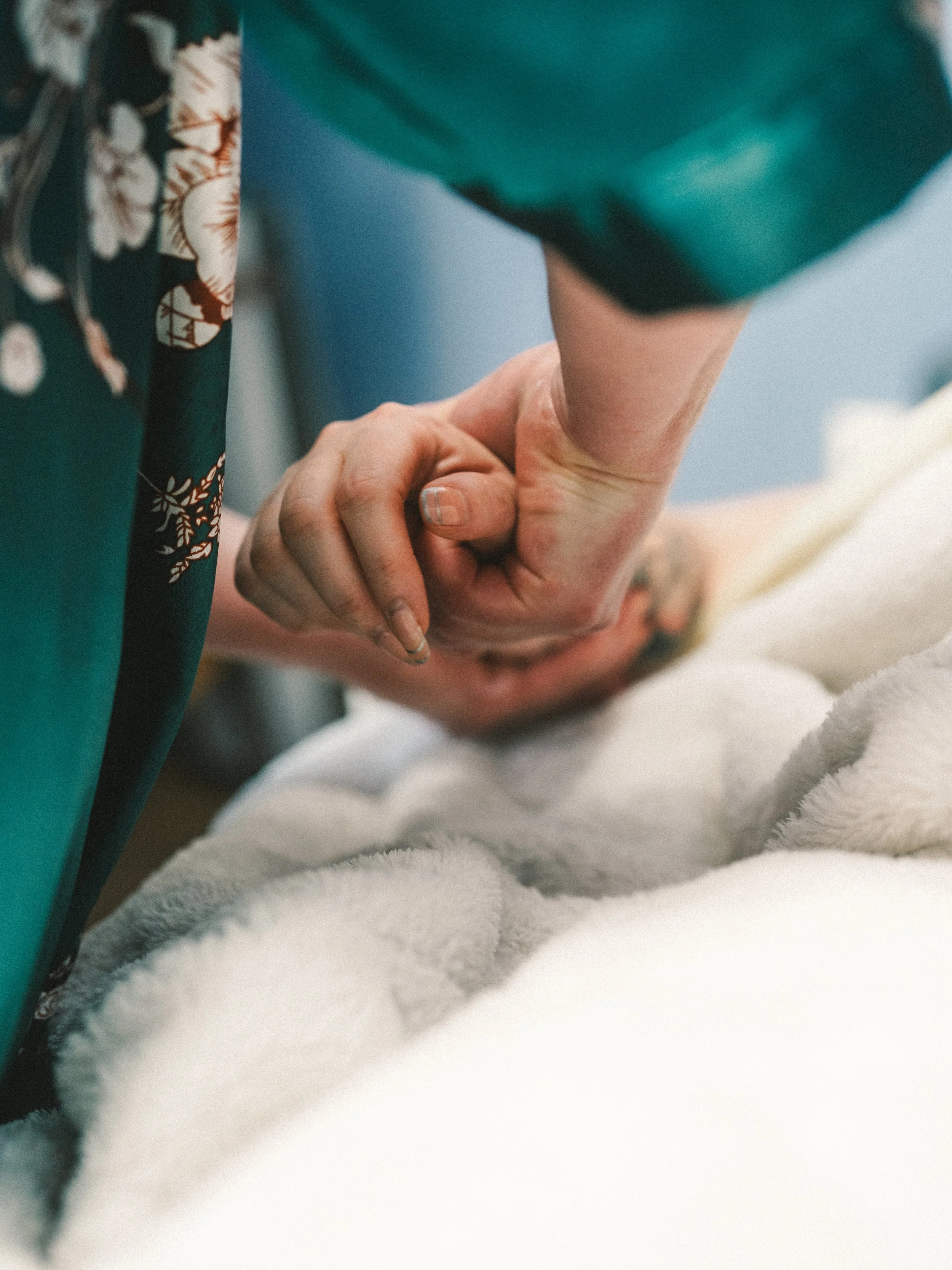A person holding another person's hand during childbirth, with the person lying on a bed covered in a white blanket.