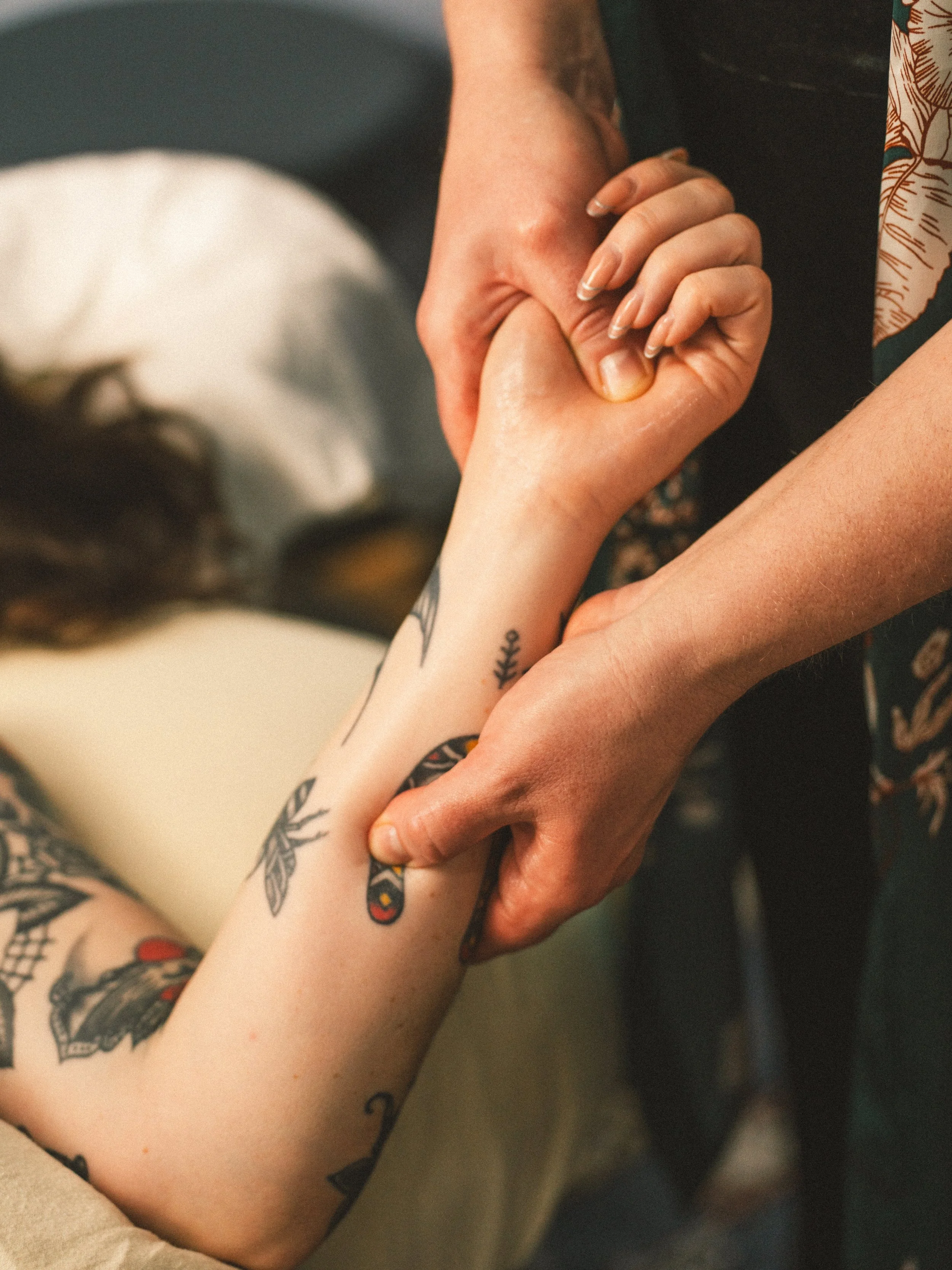 A person with tattoos on their forearm holding a person's hand.