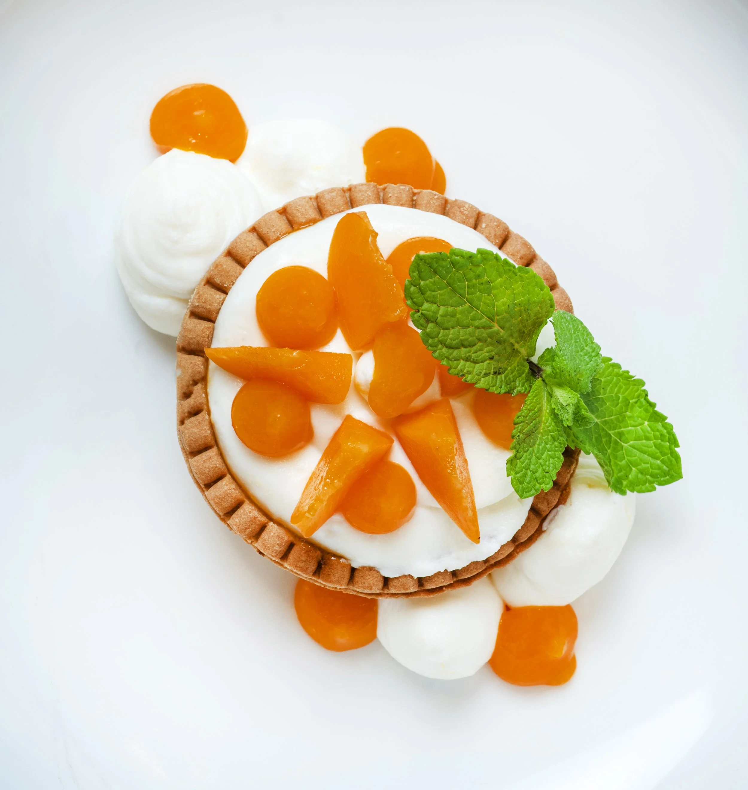 Tartelletta con crema bianca, albicocche a fette, foglie di menta e sciroppo d'acero, decorata con ciuffetti di panna.
