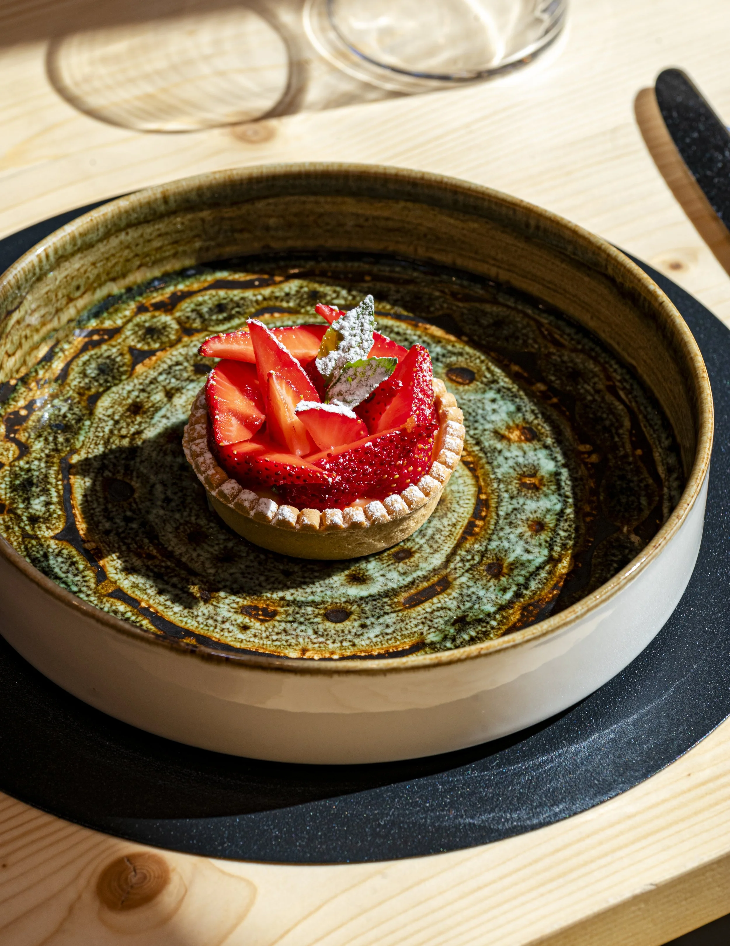 Tartellette con fragole fresche, decorata con foglioline di menta e una spolverata di zucchero a velo, servita su un piatto di ceramica decorato.