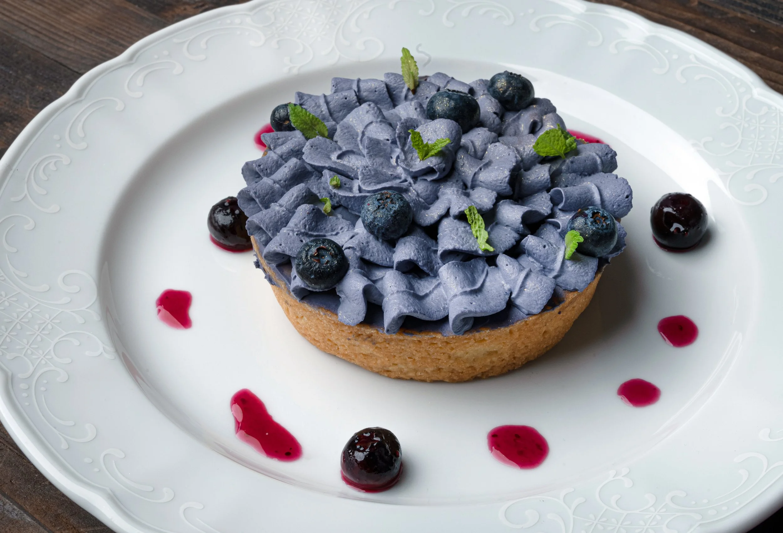Tartellette con crema di mirtilli, decorata con mirtilli freschi e foglie di menta, servita su un piatto bianco con decorazioni