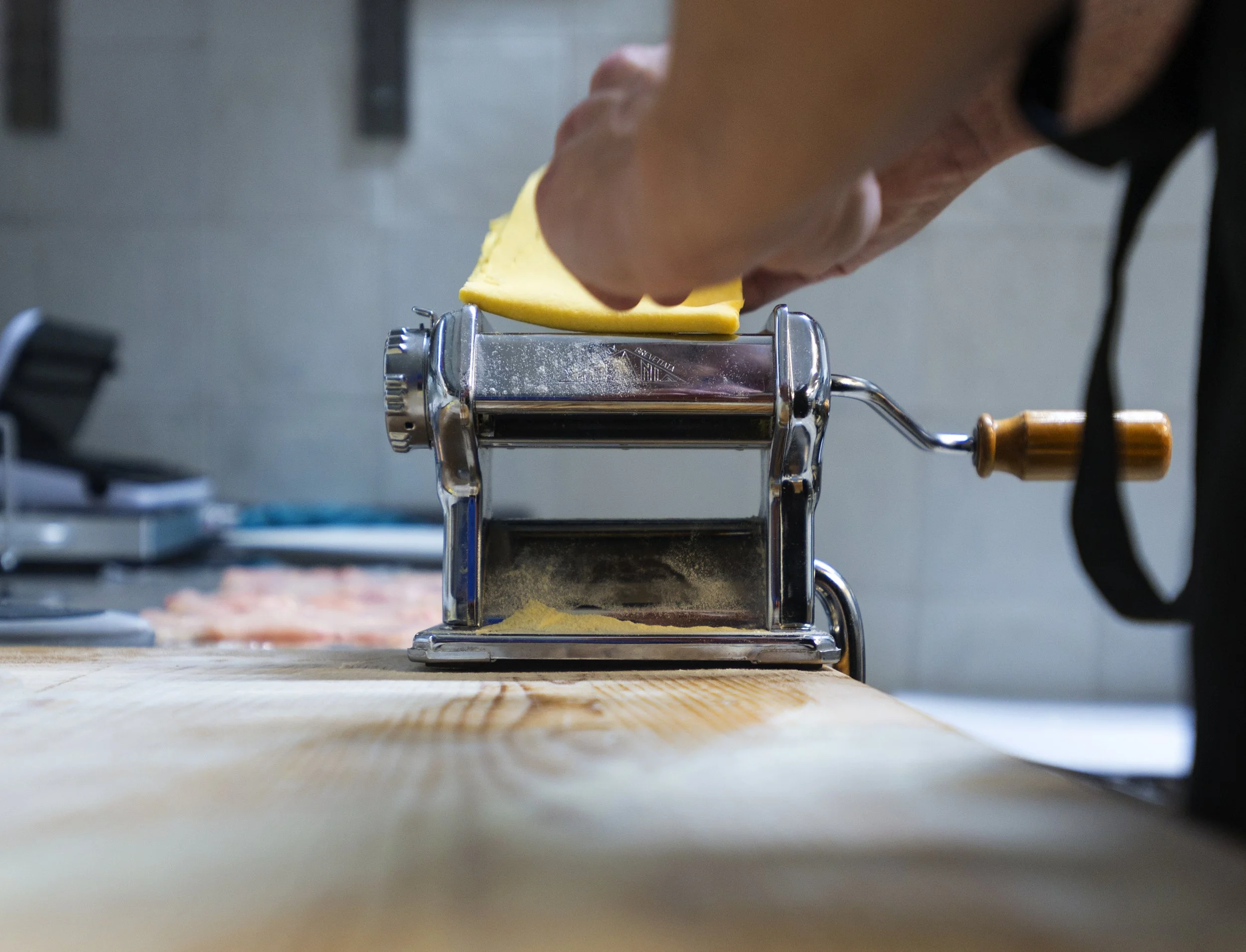 Una mano che utilizza una macchina per fare la pasta su una superficie di legno.