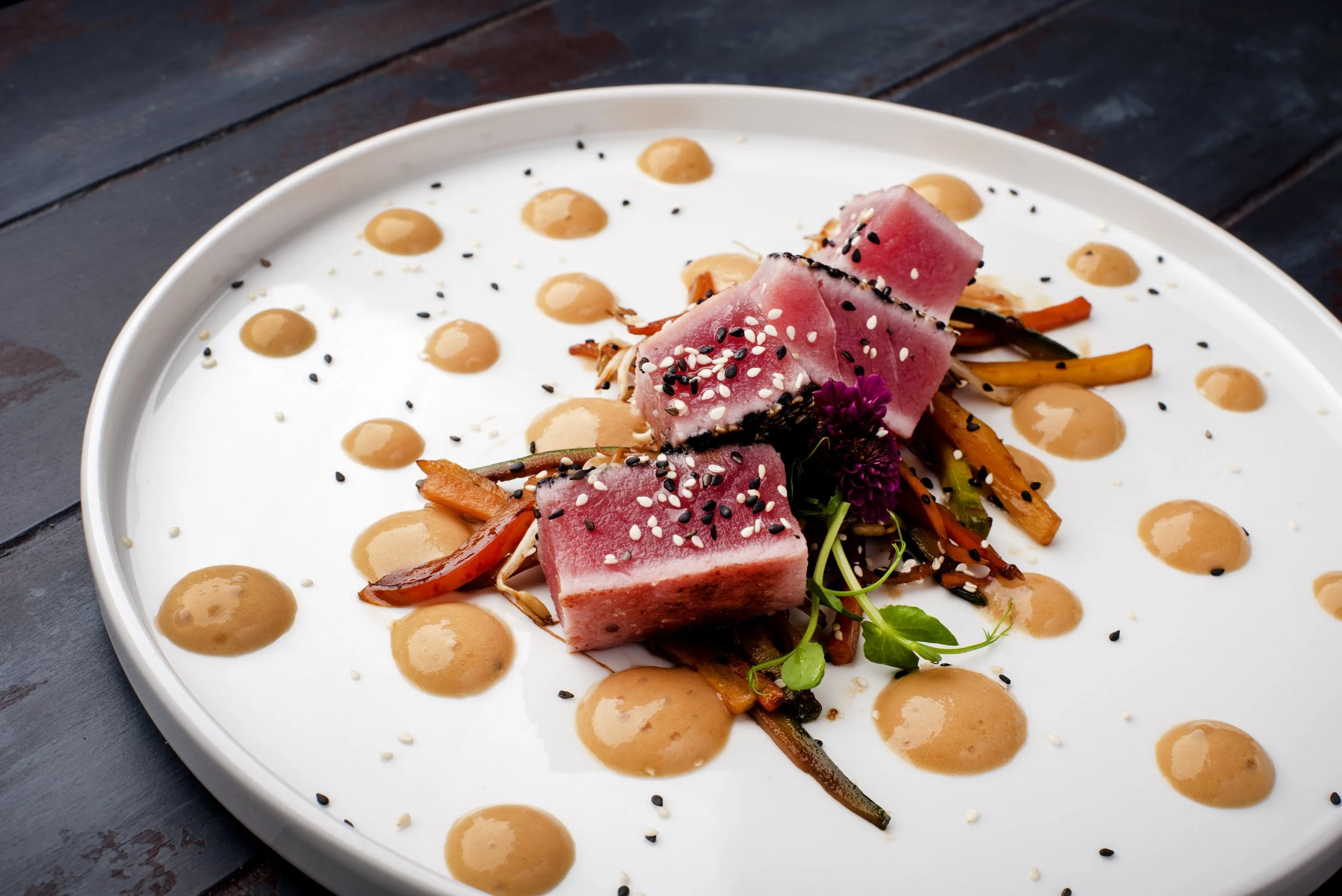 Piatti gourmet con fette di tonno rosa, guarniti con semi di sesamo nero e bianco, decorati con salsa e verdure.