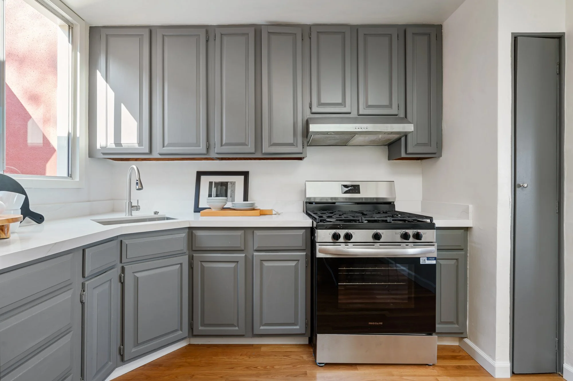 Modern kitchen with gray cabinets, white countertop, stainless steel oven, and a window with natural light.