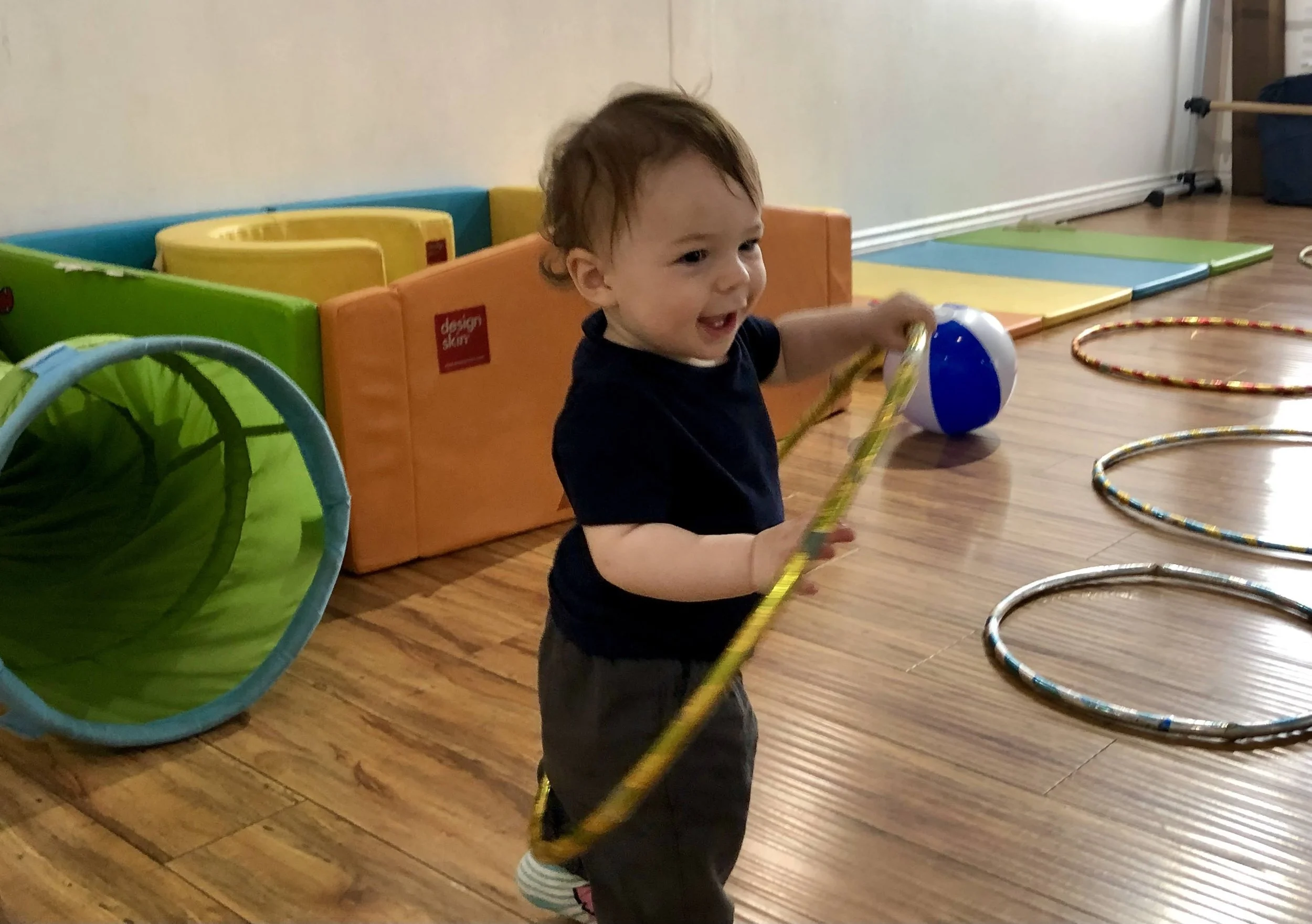 A small boy in a black t-shirt plays indoors with a gold hoola hoop