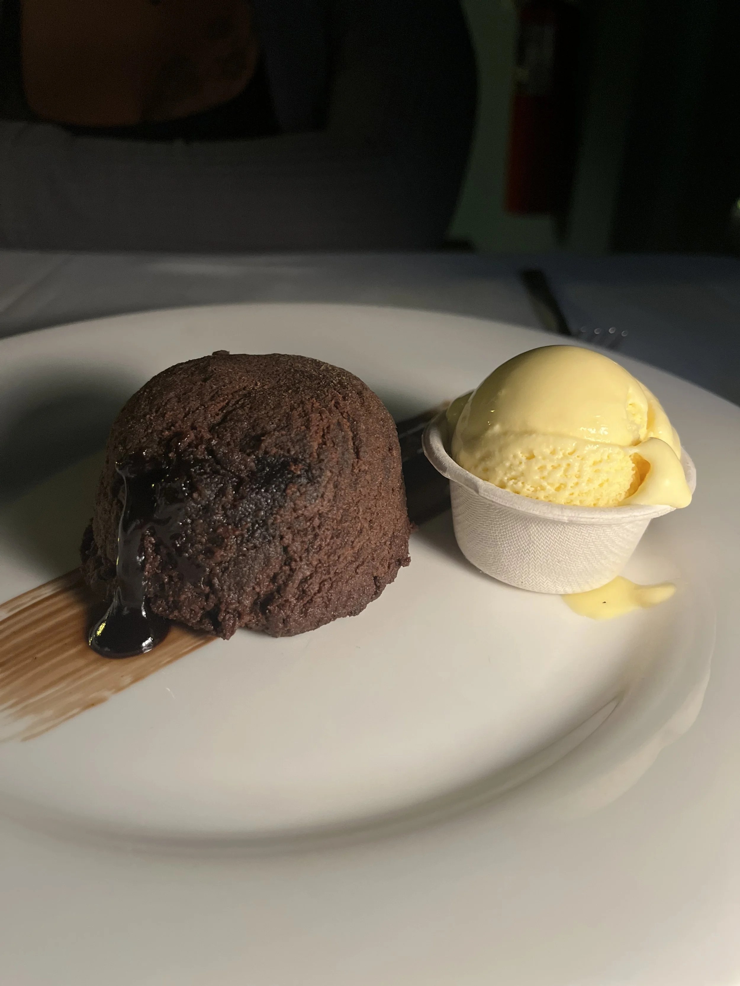 Chocolate lava cake with melted chocolate drizzle and a scoop of vanilla ice cream on a white plate.