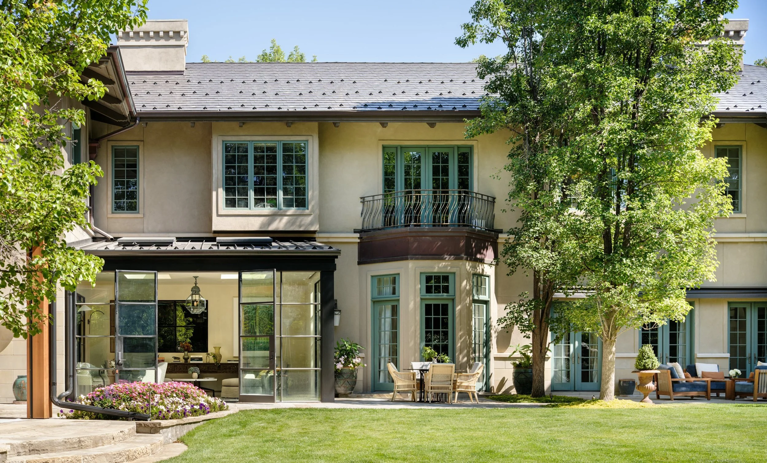 Front yard of a large two-story house with a well-maintained lawn, several trees, and an outdoor seating area with chairs and a table. Charleston interior designer Sarah Hart Interior Design. 