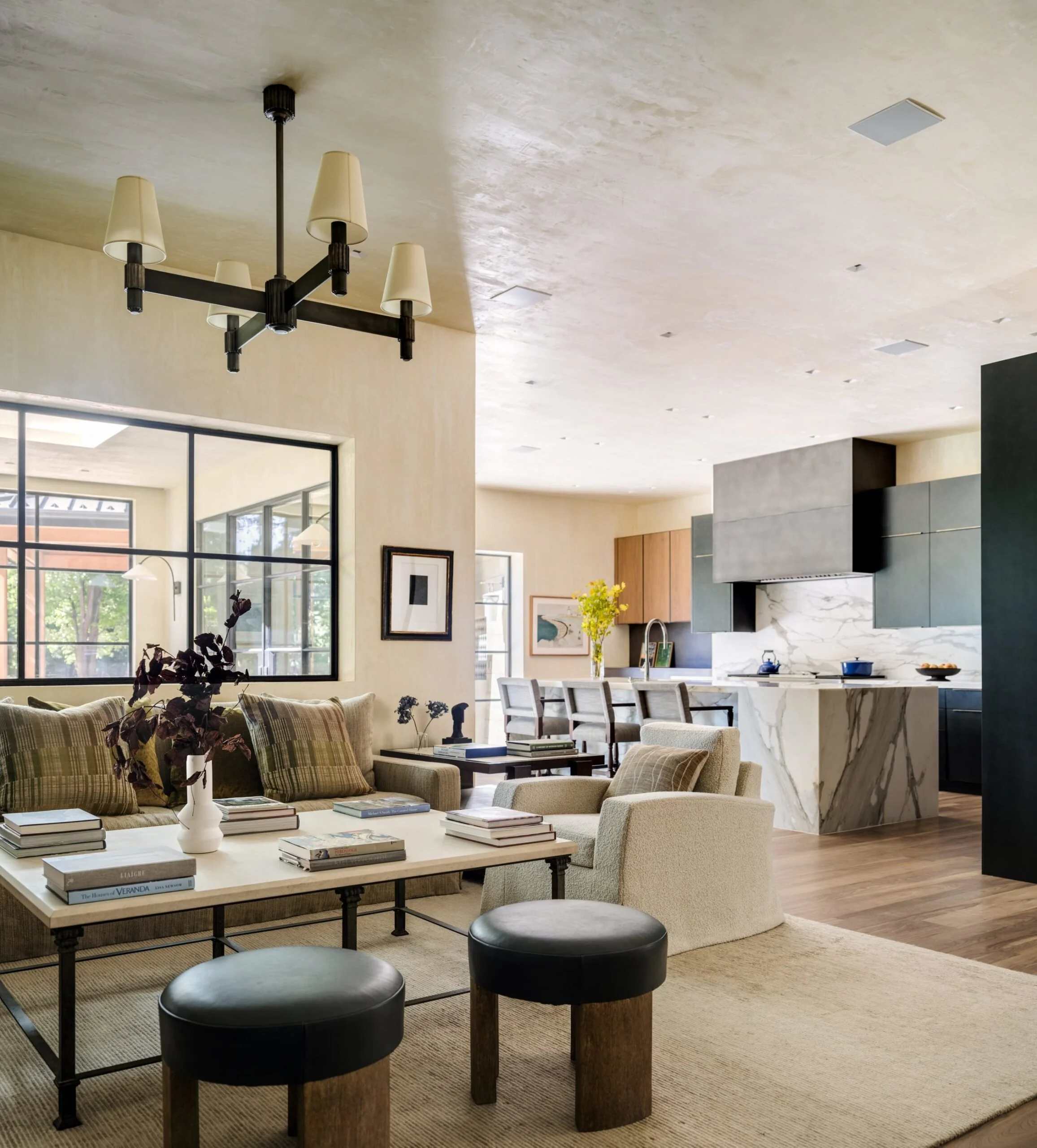 Open-concept living room and kitchen with modern decor, large window, and chandelier lighting. Formations Sofa, Holland and Sherry Rug. Rose Tarlow. Wolf Subzero. Custom cabinets. Architectural Digest inspired interiors. Charleston Interior Designer.