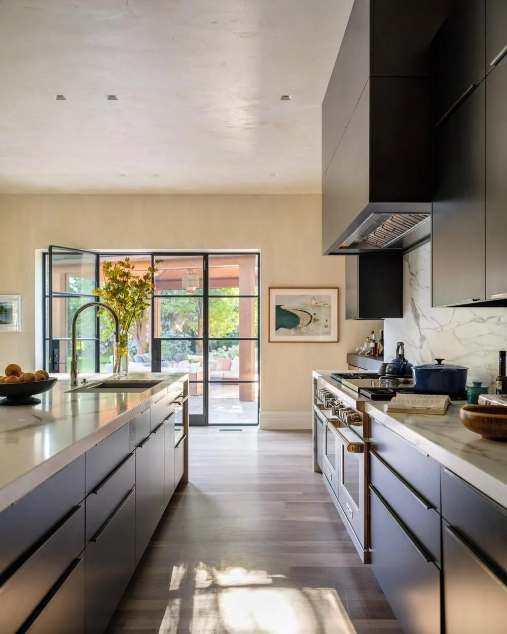 Modern kitchen with black cabinetry, marble countertops, and a large window overlooking a patio with greenery. Charleston interior designer Sarah Hart Interior Design. 