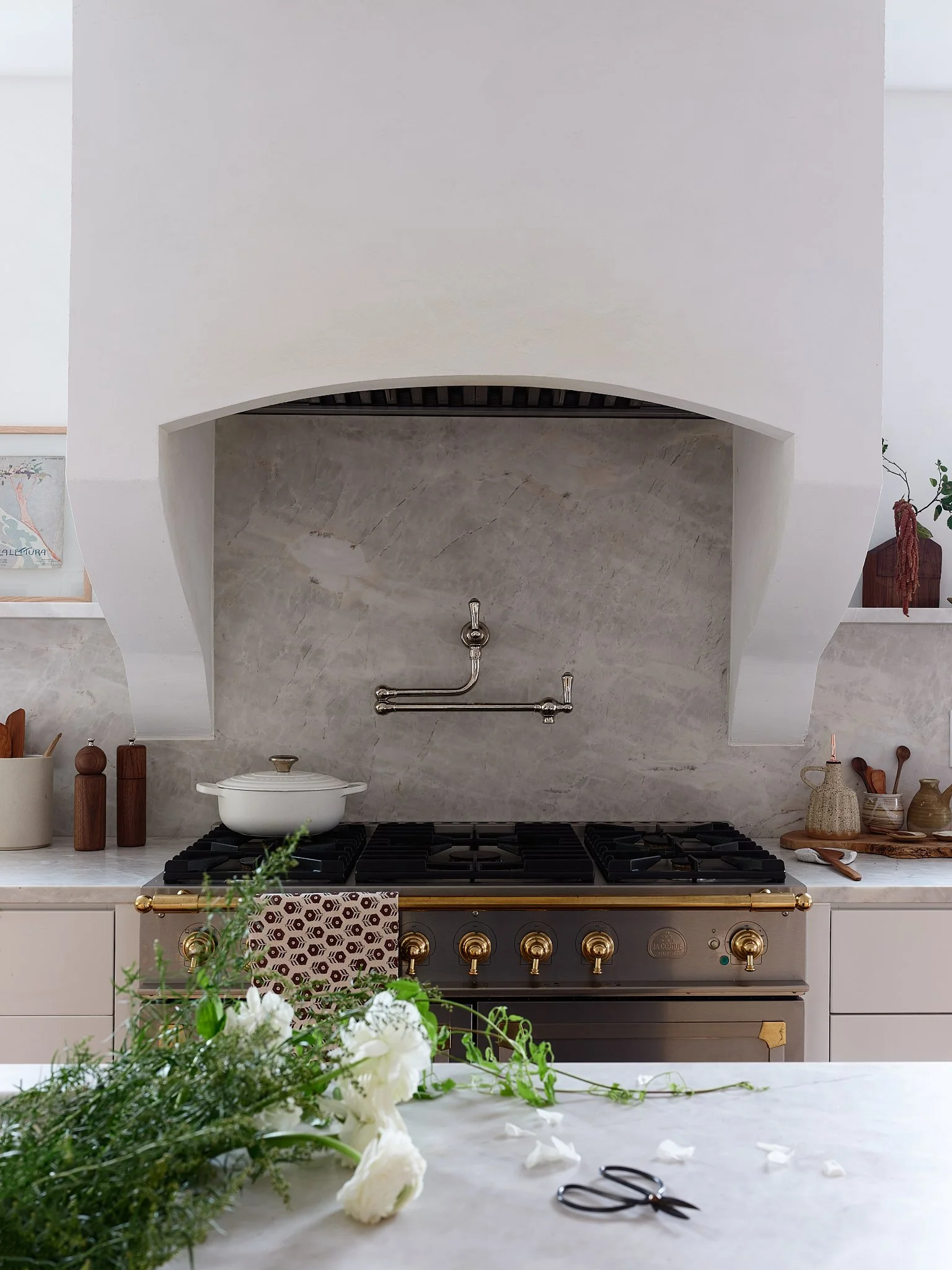 Modern kitchen with white marble countertop, stainless steel stove, and decorative shelves with plants and pottery.