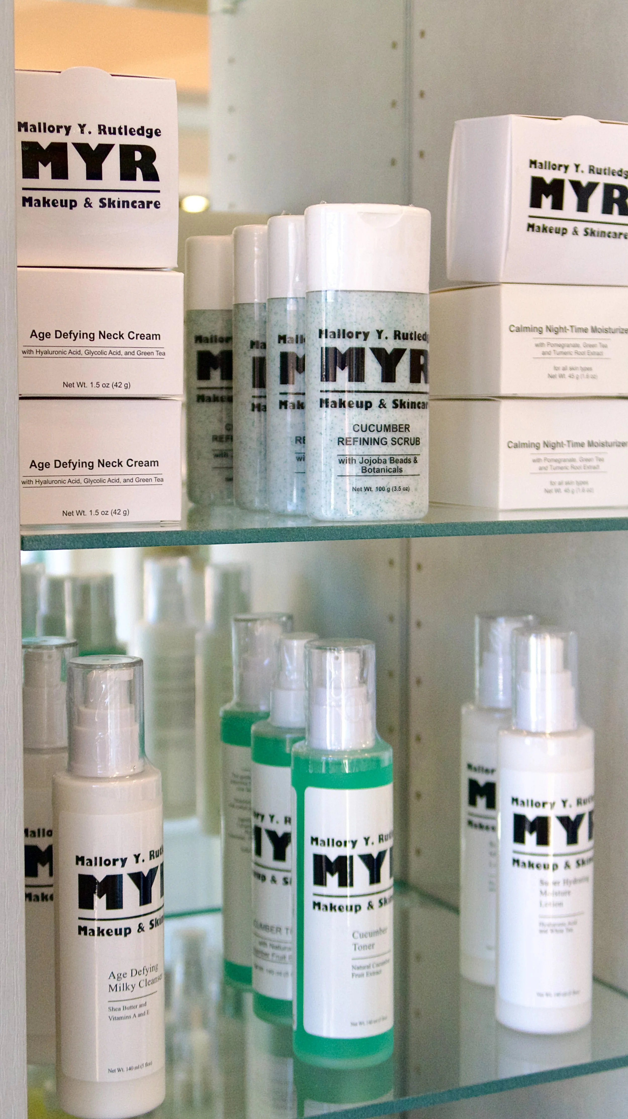  shelves with skincare products including age defying neck cream, cucumber refining scrub, calming night-time moisturizer, cucumber toner, and milky cleanser, all from MYR Makeup & Skincare by Mallory Y. Rutledge.