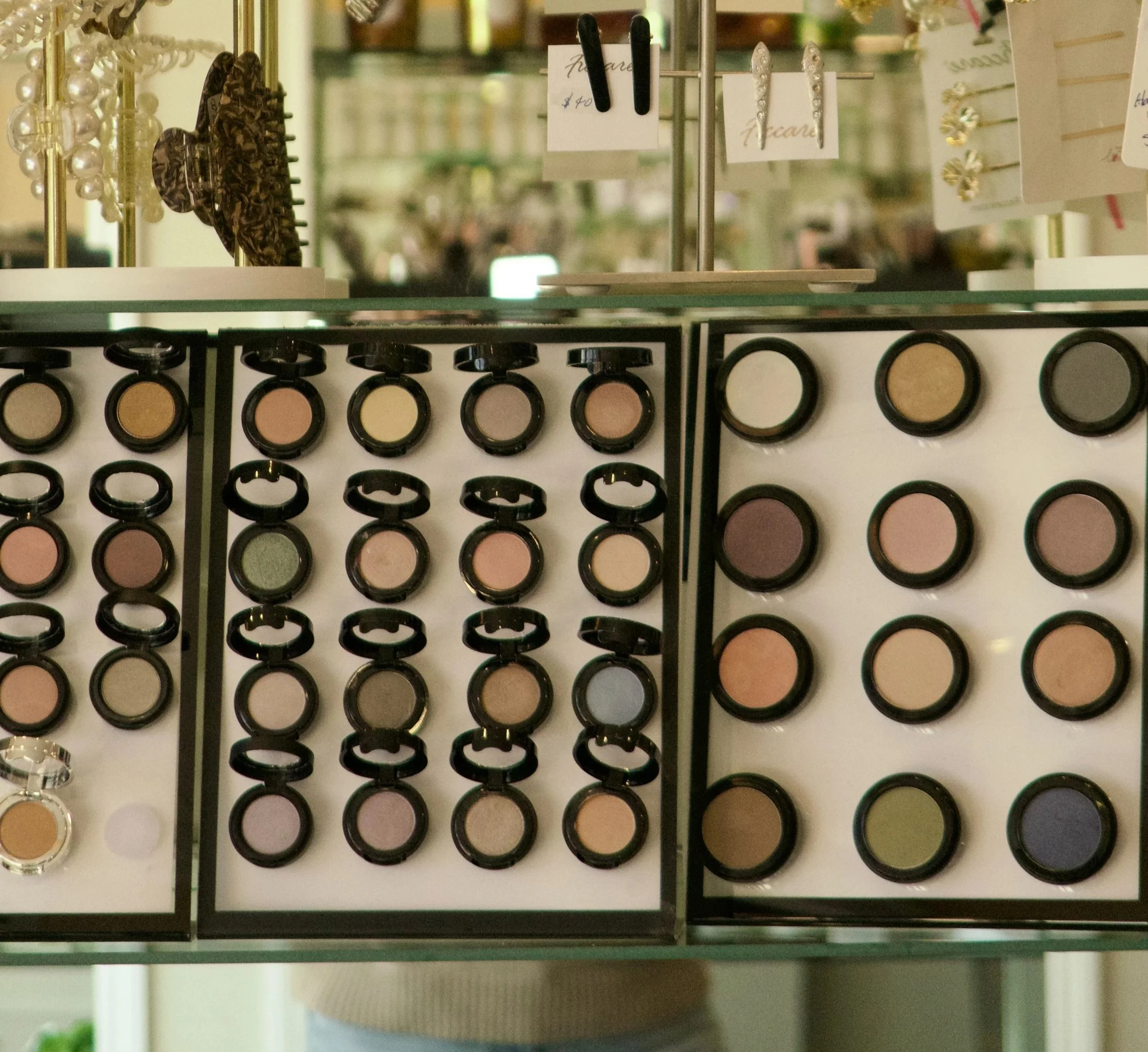 Display of various eyeshadows in circular pans, arranged in rows and columns in a makeup store.
