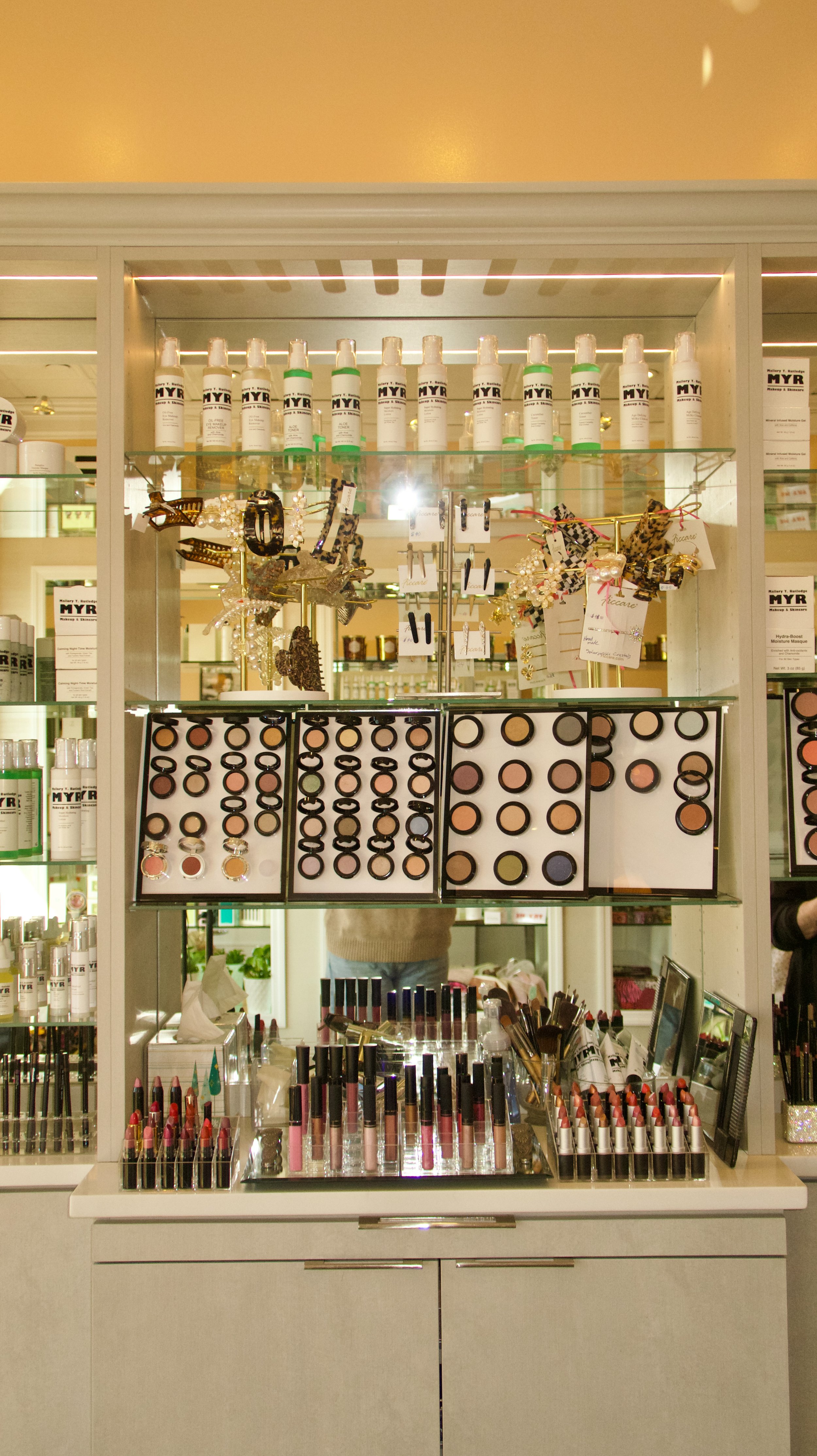 A display of makeup and beauty products including lipstick, compact powders, and skincare bottles in a store.