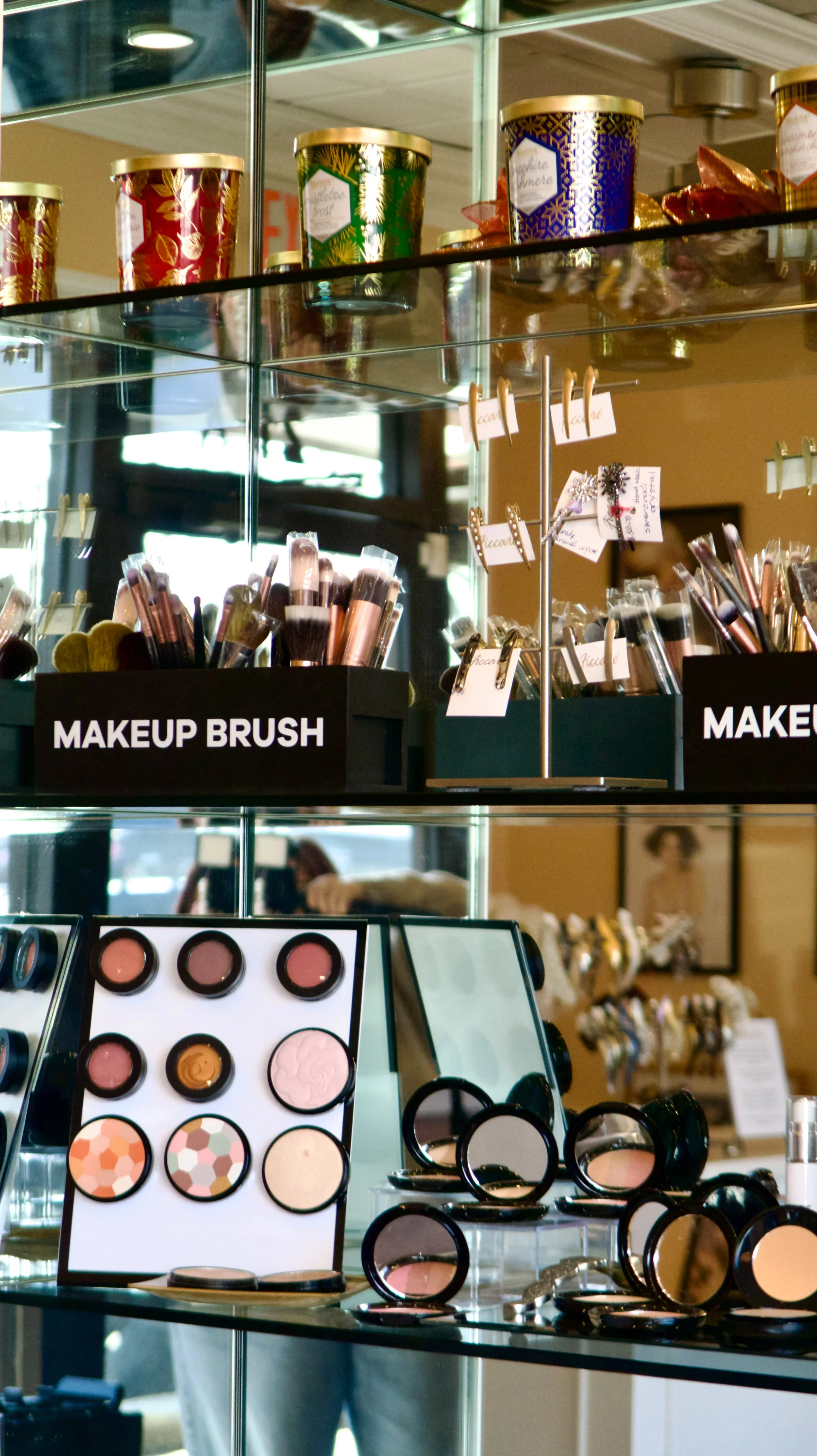 Display of makeup brushes, compacts, and cosmetics in a store with shelves labeled 'MAKEUP BRUSH' and various makeup products arranged on glass shelves.