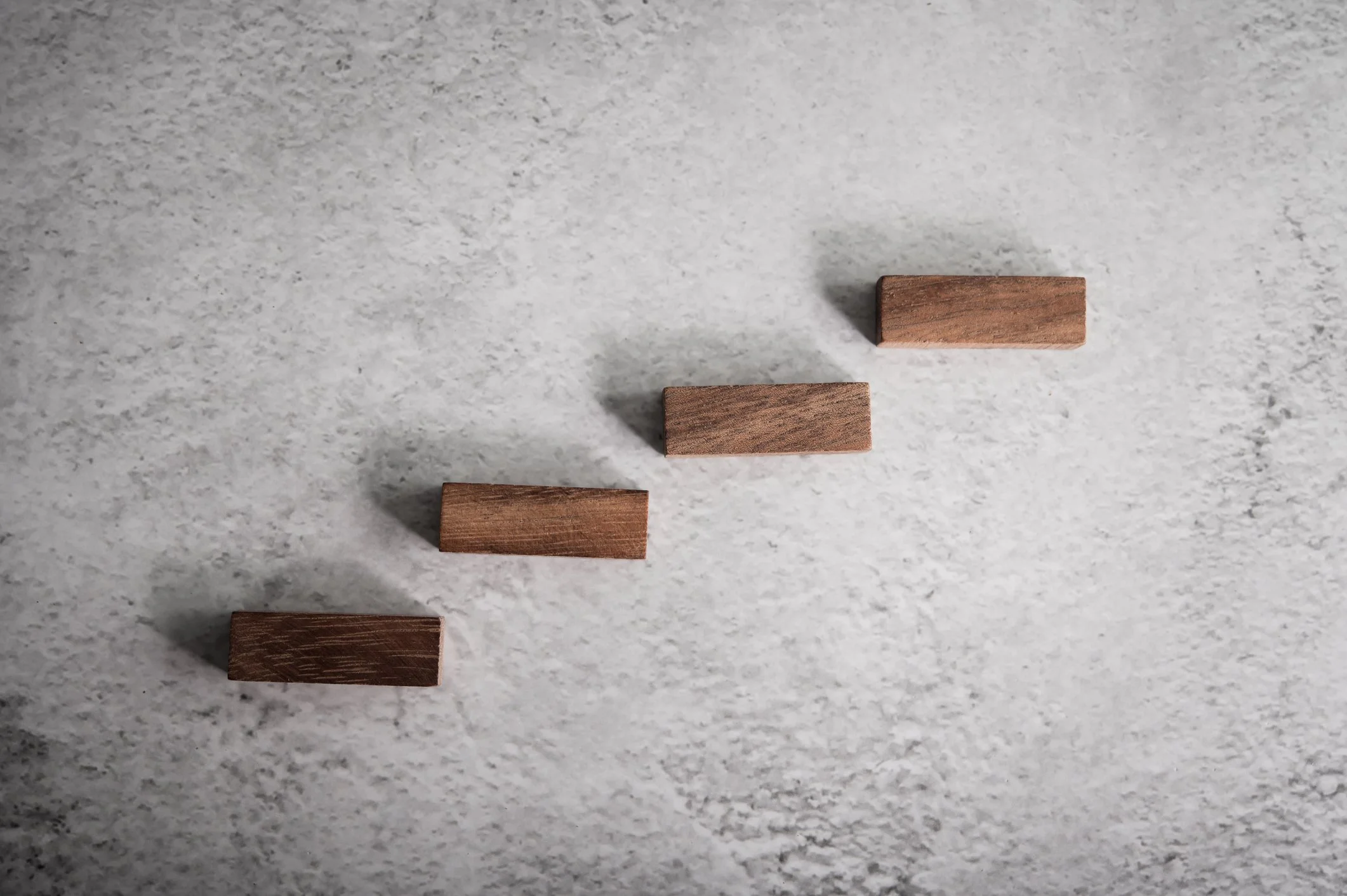 Four small wooden blocks arranged diagonally on a textured light gray surface.