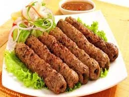 Nine grilled meat kebabs with a side of sliced onion and a small bowl of dipping sauce on a white plate