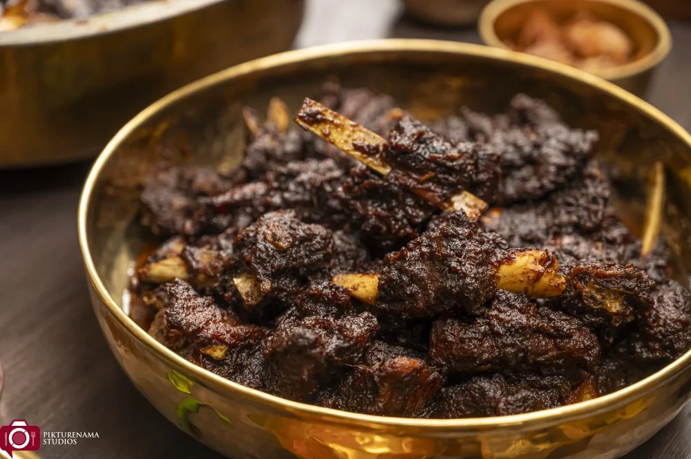 A bowl of cooked, dark brown, spicy meat stew with visible bone segments.