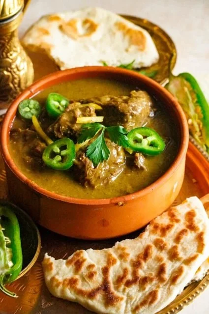 Indian curry with meat garnished with sliced green chilies and cilantro, served with naan bread and a side salad.