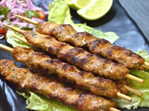 Close-up of grilled meat skewers on a plate with lettuce and lime wedges.