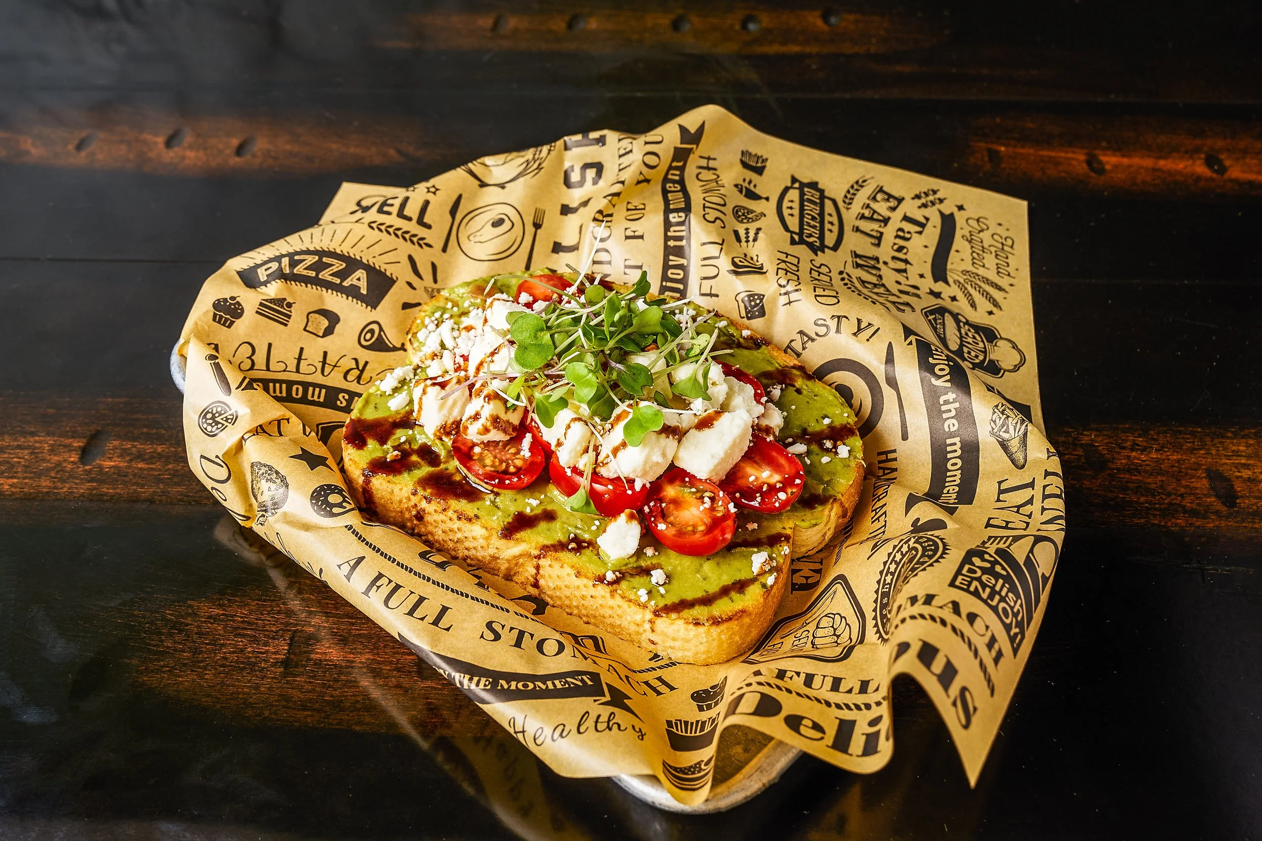 Avocado toast with cherry tomatoes, feta, microgreens, and balsamic drizzle on deli paper — restaurant food photography by BK Captured
