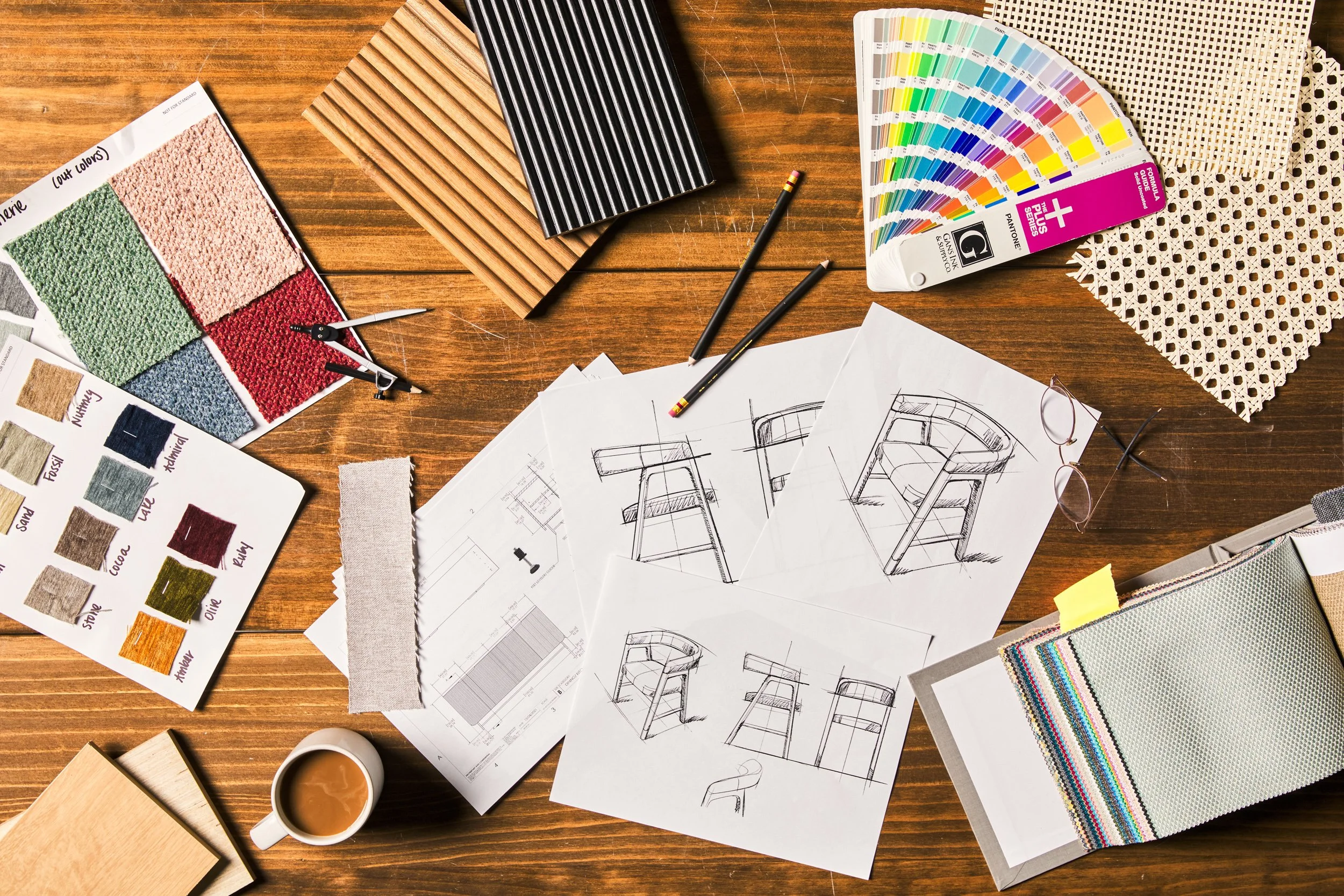 Overhead flatlay of furniture blueprints, fabric swatches, and color samples on wood surface — interior design product photography by BK Captured