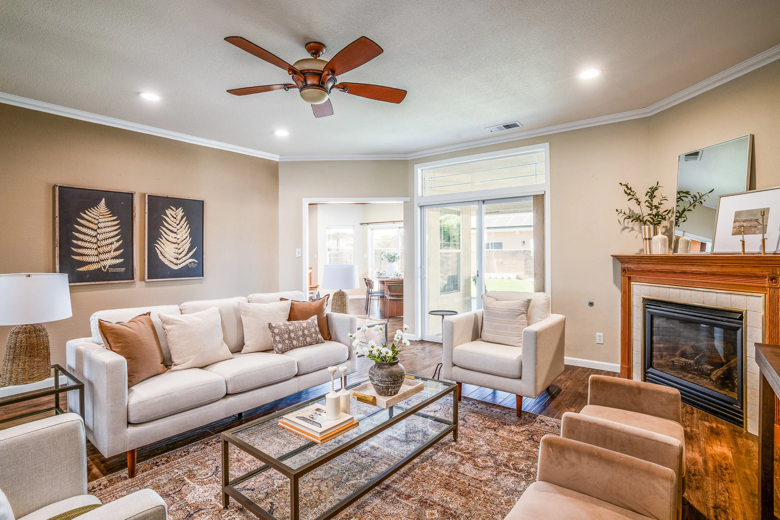 Staged living room with a cream sofa, framed fern prints, gas fireplace, and view to the dining room