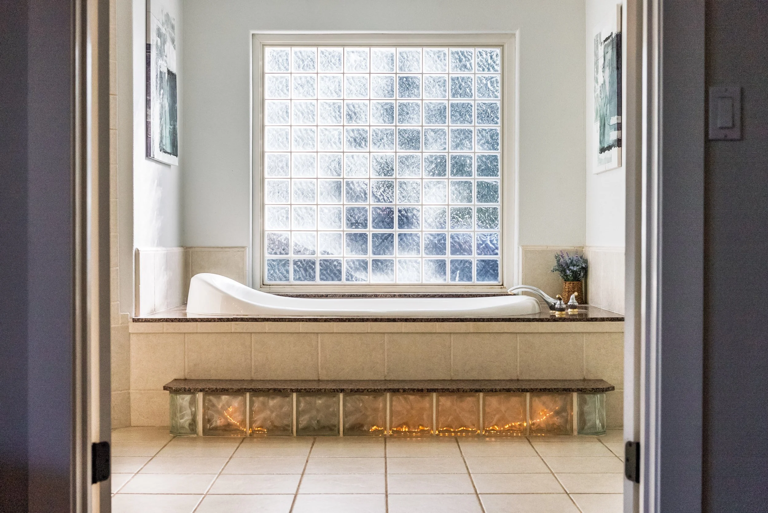 Spa-like bathroom with a soaking tub framed by a glass-block window and warm accent lighting