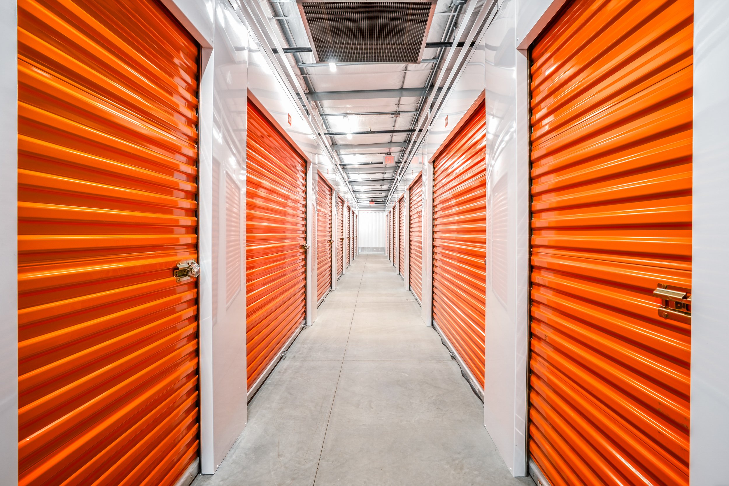 Interior corridor of Porterville self-storage facility with rows of orange roll-up doors and polished concrete floors — commercial architectural photography by BK Captured