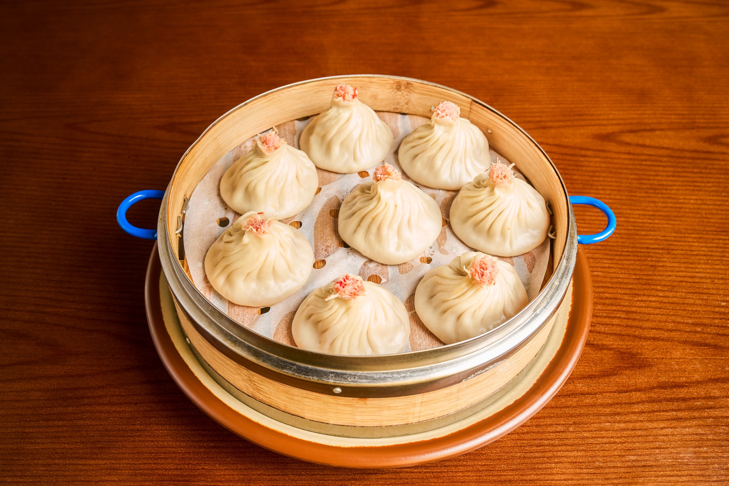 Crab and pork soup dumplings in bamboo steamer basket on warm wood table — restaurant menu photography by BK Captured