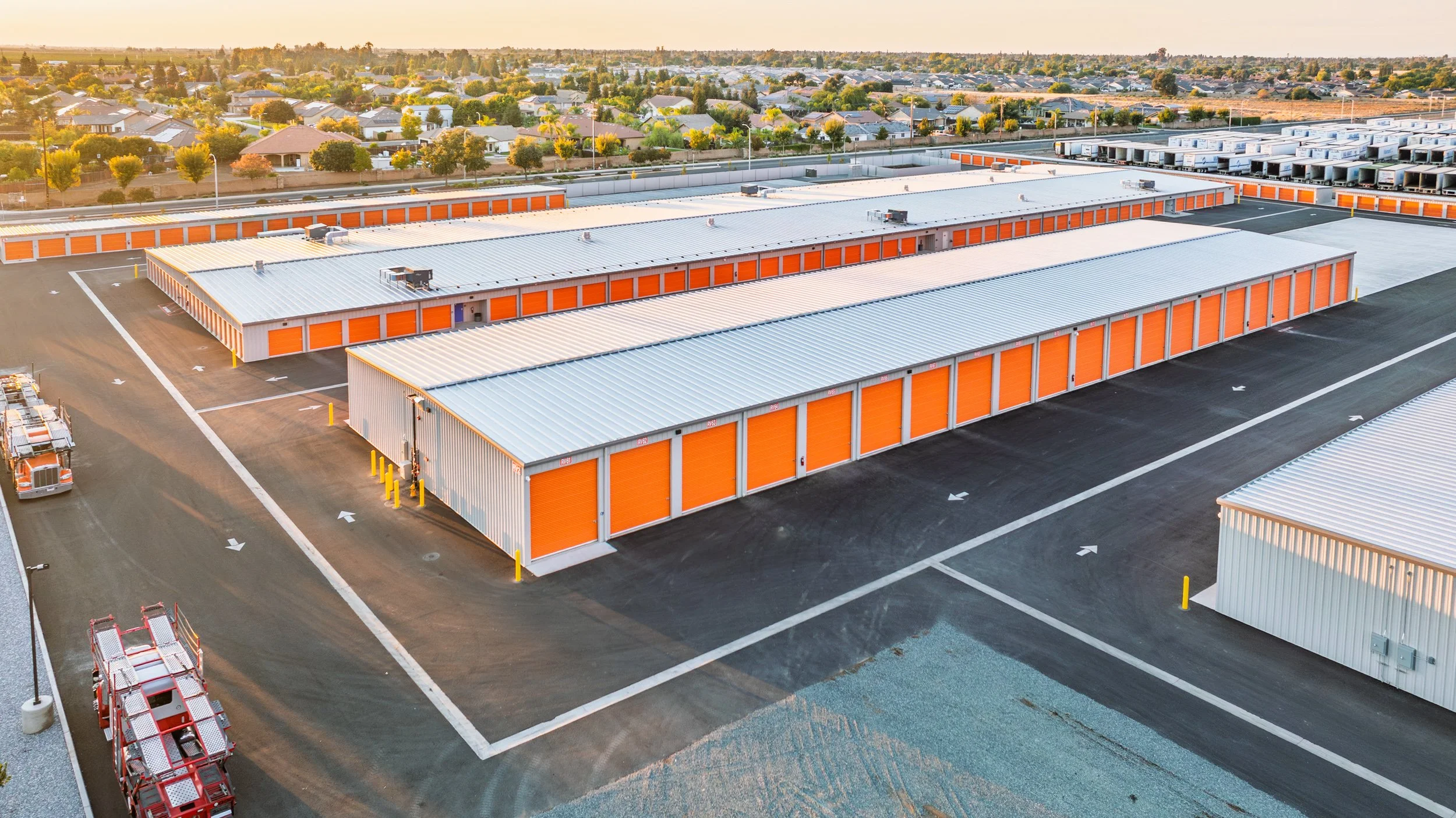 Aerial view of a self-storage facility with long rows of orange-door units at golden hour