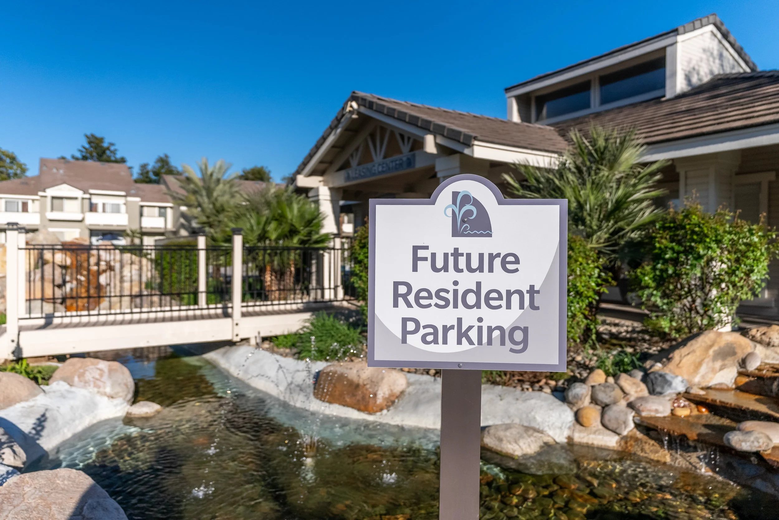 Apartment community leasing center entrance with a "Future Resident Parking" sign beside a landscaped stream and footbridge