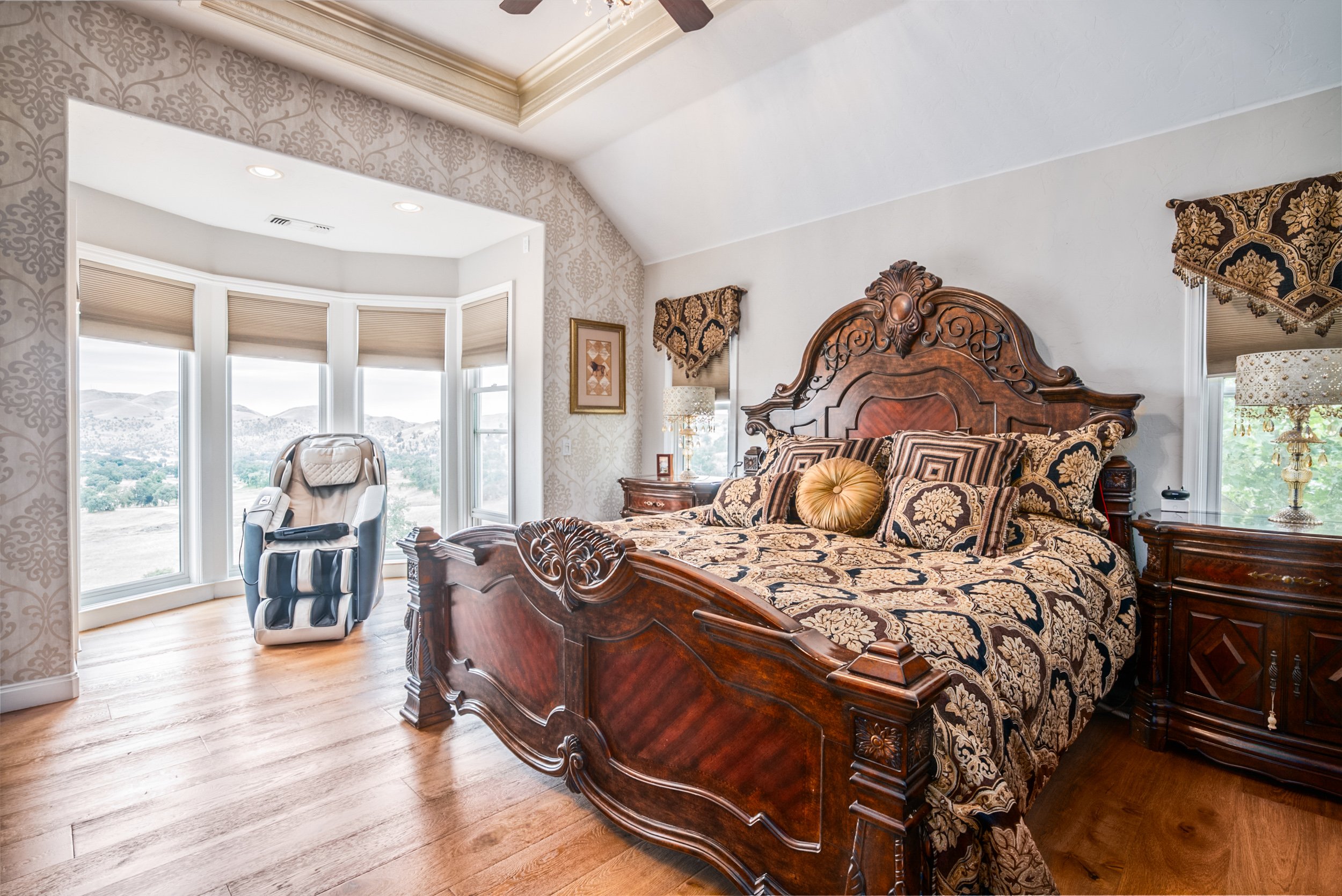 Primary bedroom with ornately carved wood bed and a bay window framing foothill views