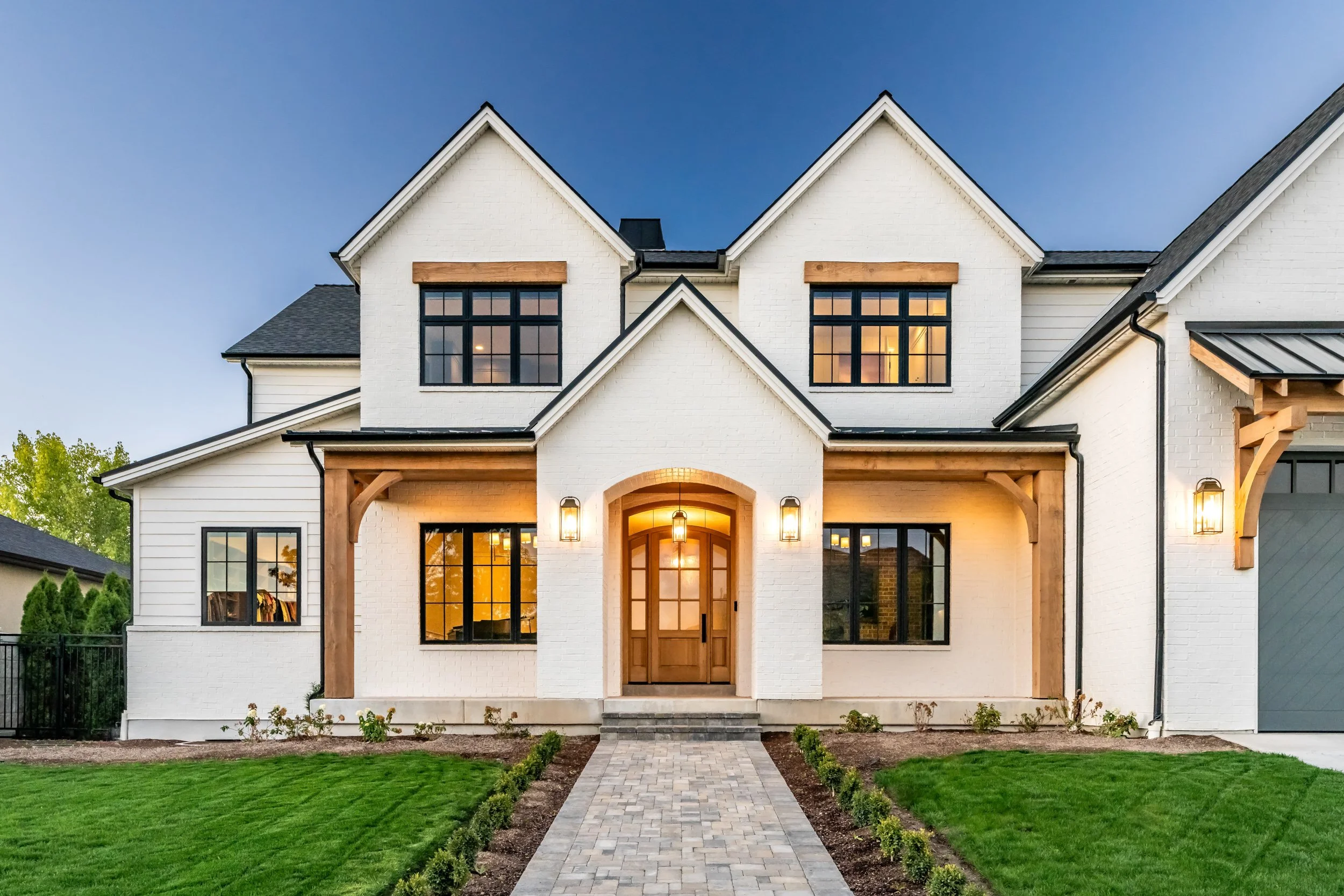 White farmhouse-style custom home exterior with black windows and three-car garage — residential architectural photography by BK Captured