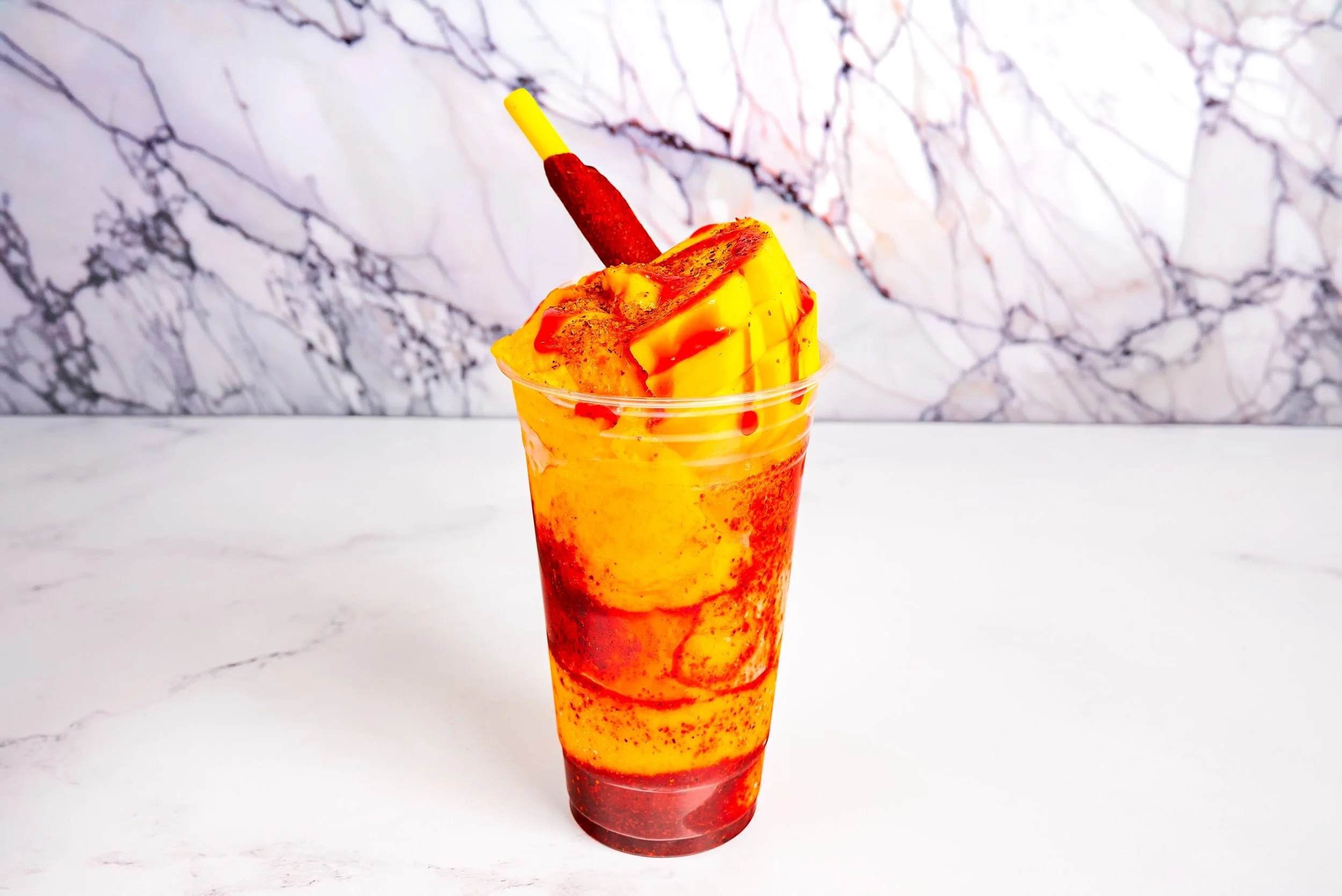 Mangonada with fresh mango, chamoy sauce, and chili-dusted tamarind straw on white marble — Mexican beverage photography by BK Captured