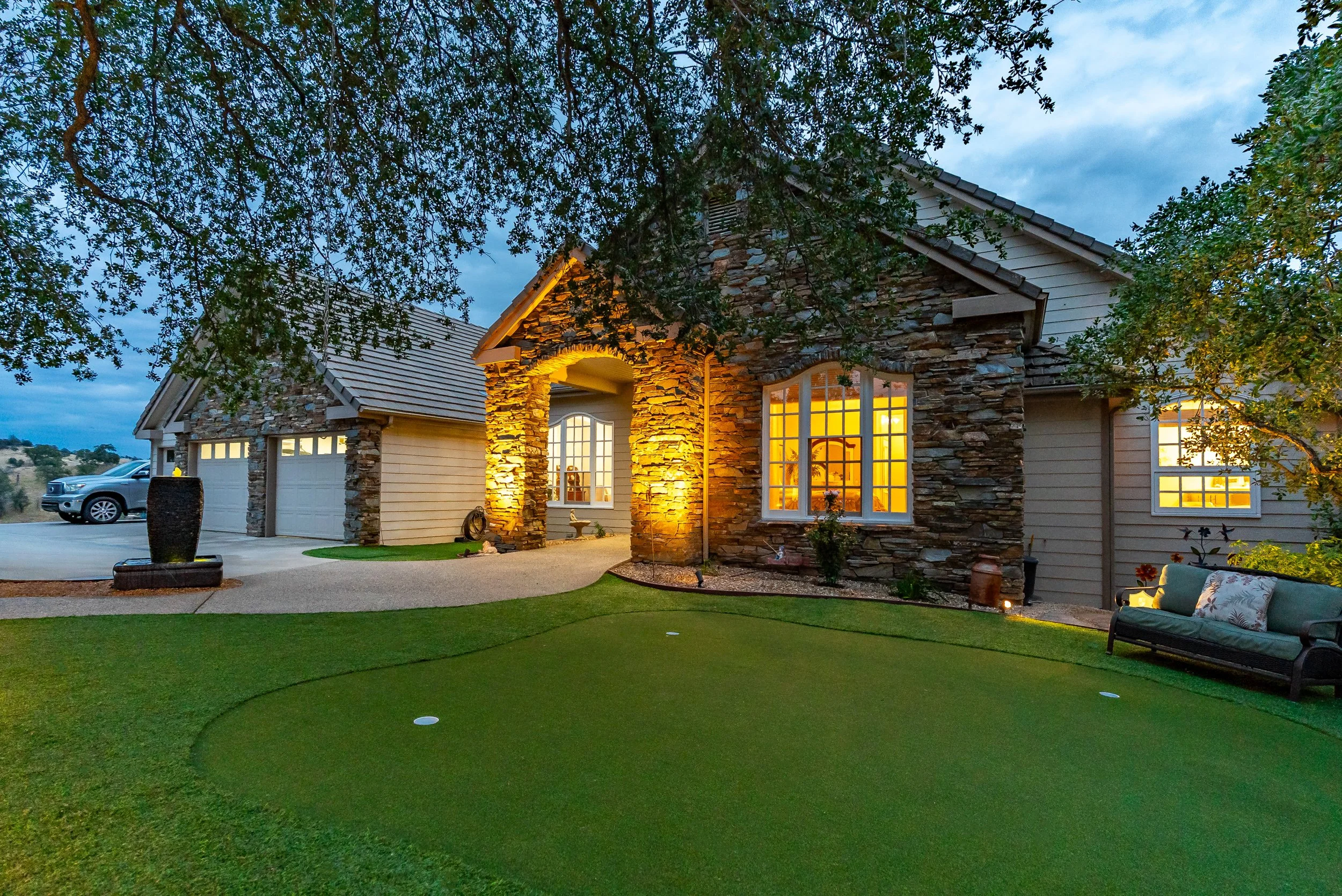 Stone-and-shingle luxury home at twilight with glowing windows and a putting-green front lawn in Brighton Crest, Friant