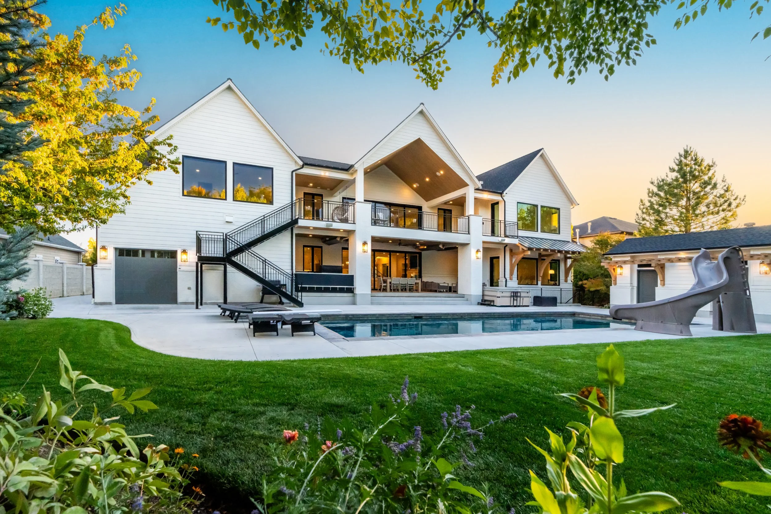 White farmhouse-style custom home exterior with deck, pool and landscaping at sunset — residential architectural photography by BK Captured