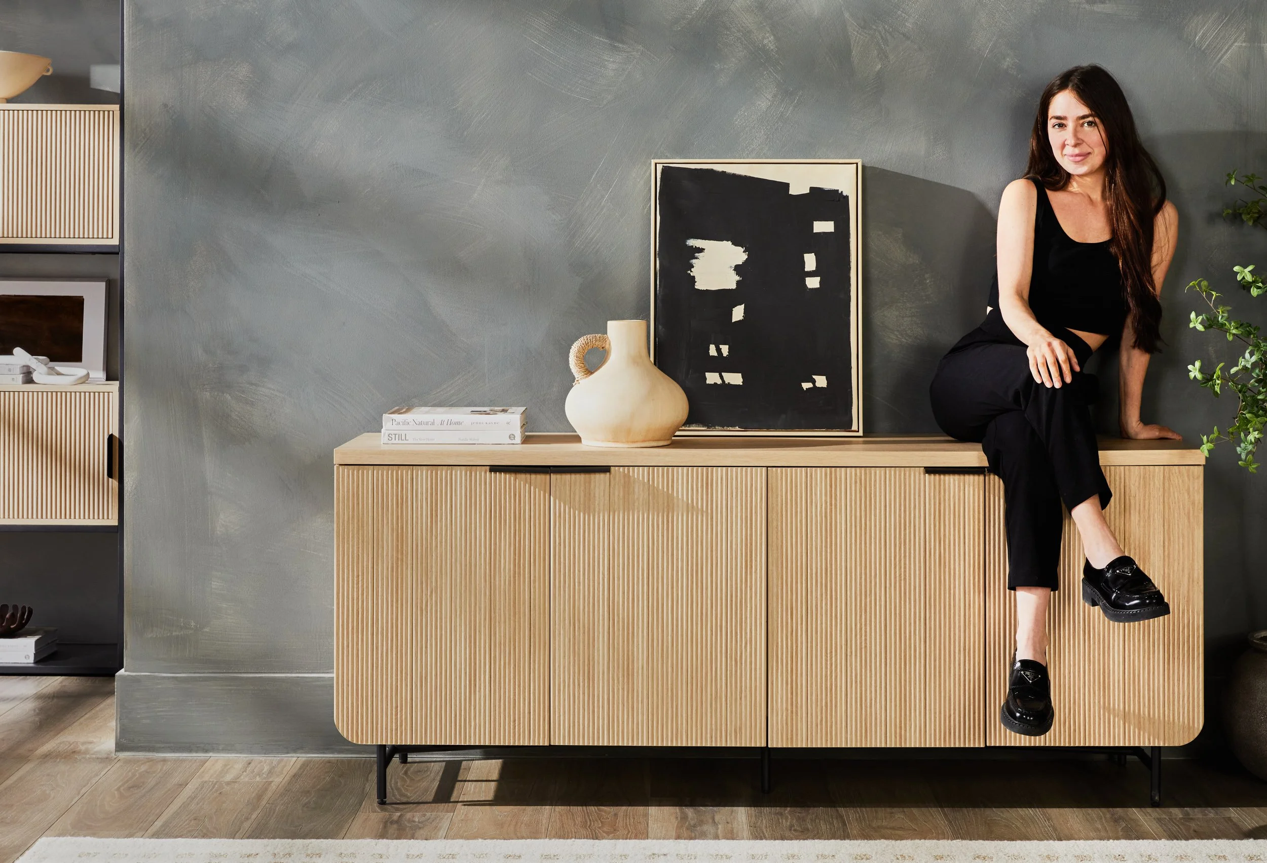 Designer seated on Walker Edison wood sideboard in styled living room with neutral tones and wall art — lifestyle furniture photography by BK Captured