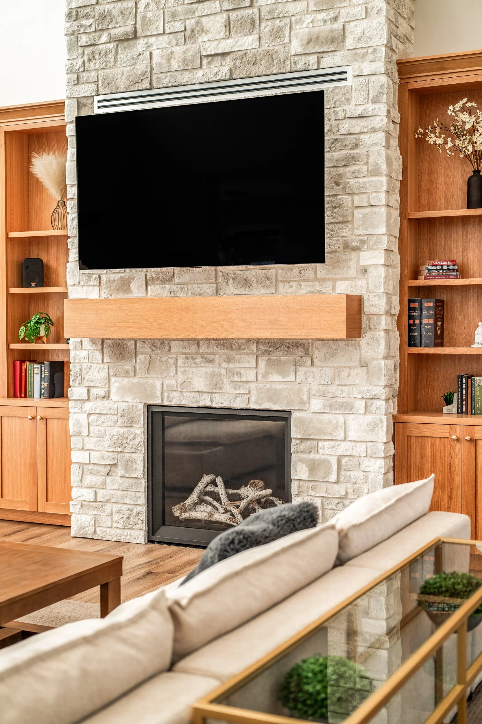 Custom built-in bookcase flanking stone fireplace with mounted TV in luxury home — interior architectural photography by BK Captured