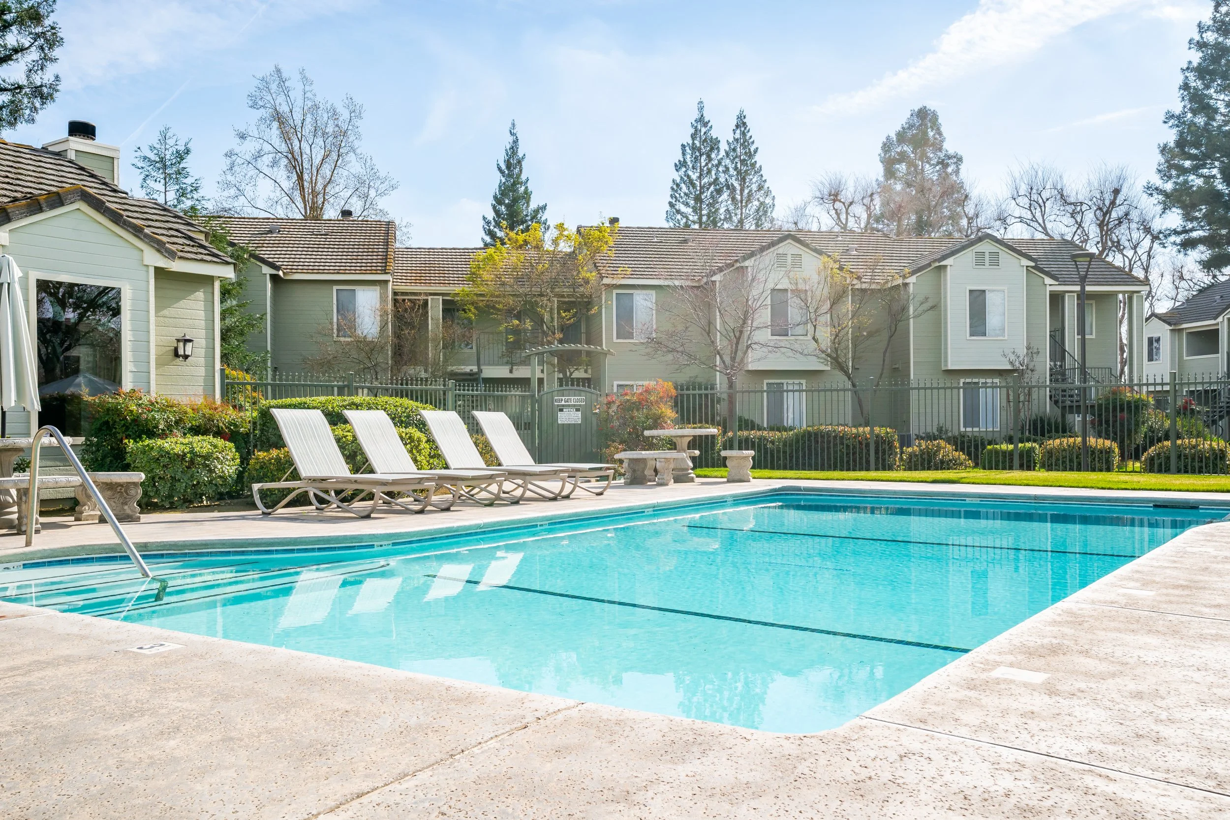 Resort-style community pool with lounge chairs framed by green two-story townhomes