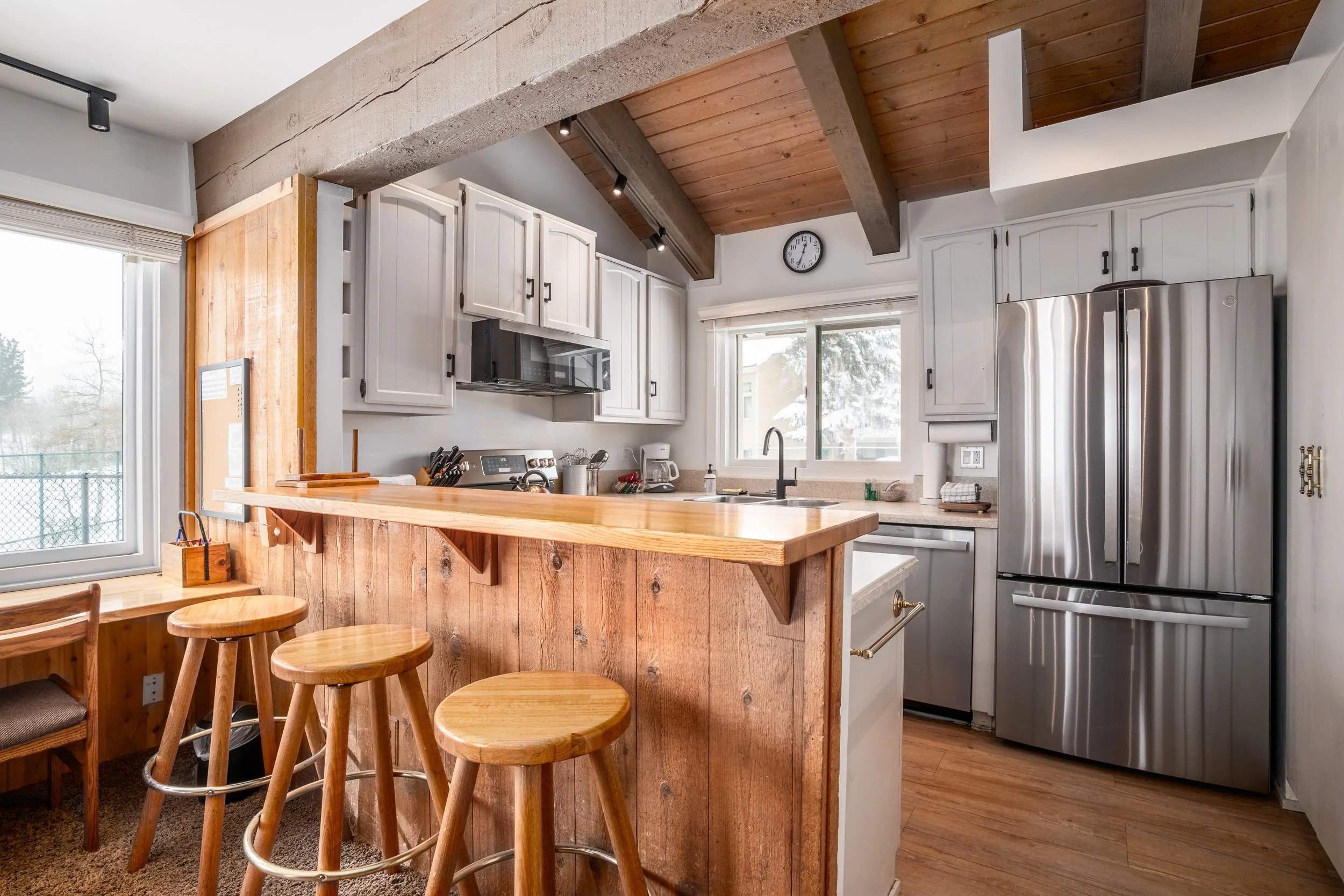 Kitchen with white cabinets, stainless steel refrigerator, tile backsplash, wooden ceiling, and a breakfast bar with wooden stools.