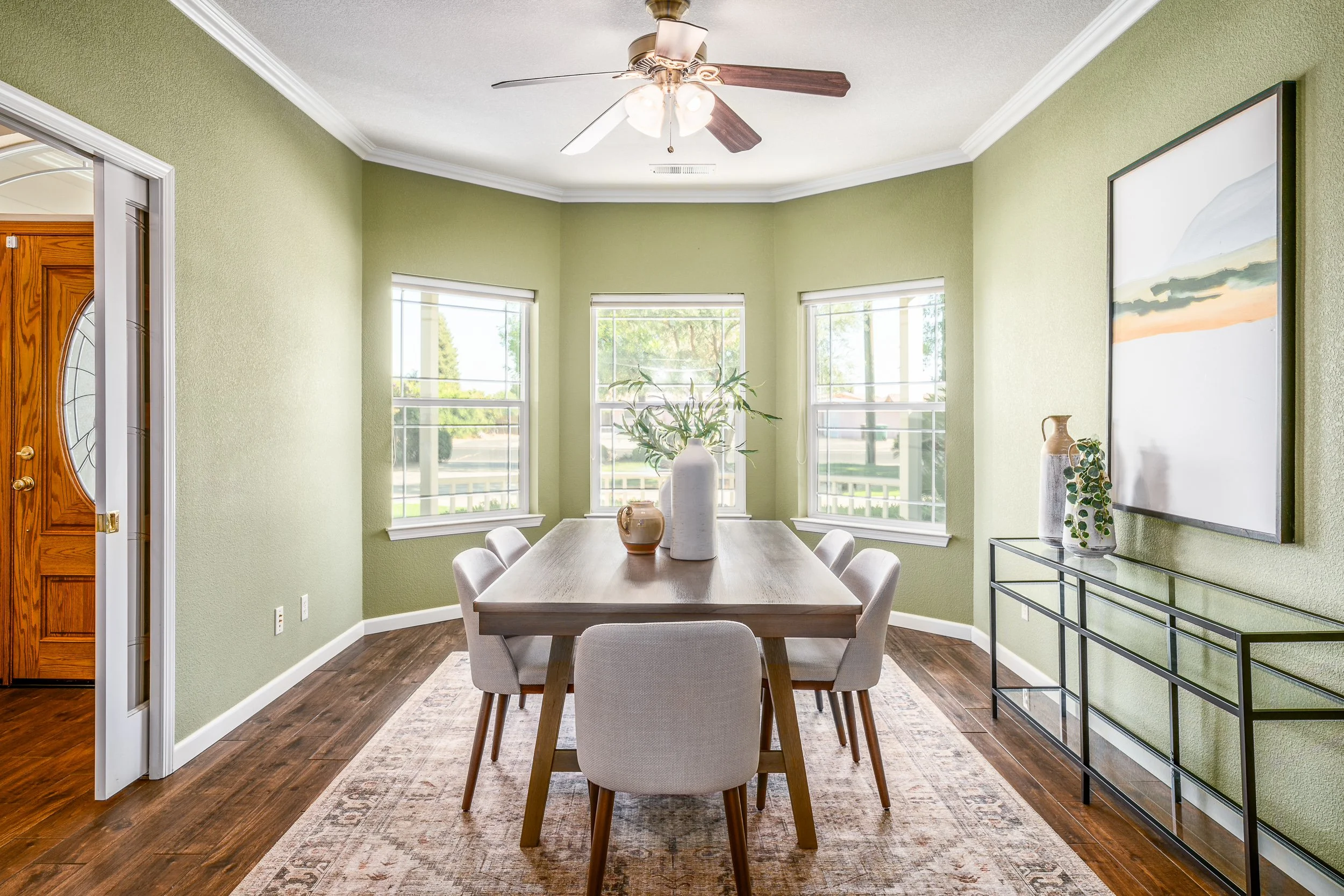 Green-walled dining room with a wood table, upholstered chairs, and a bayed window nook