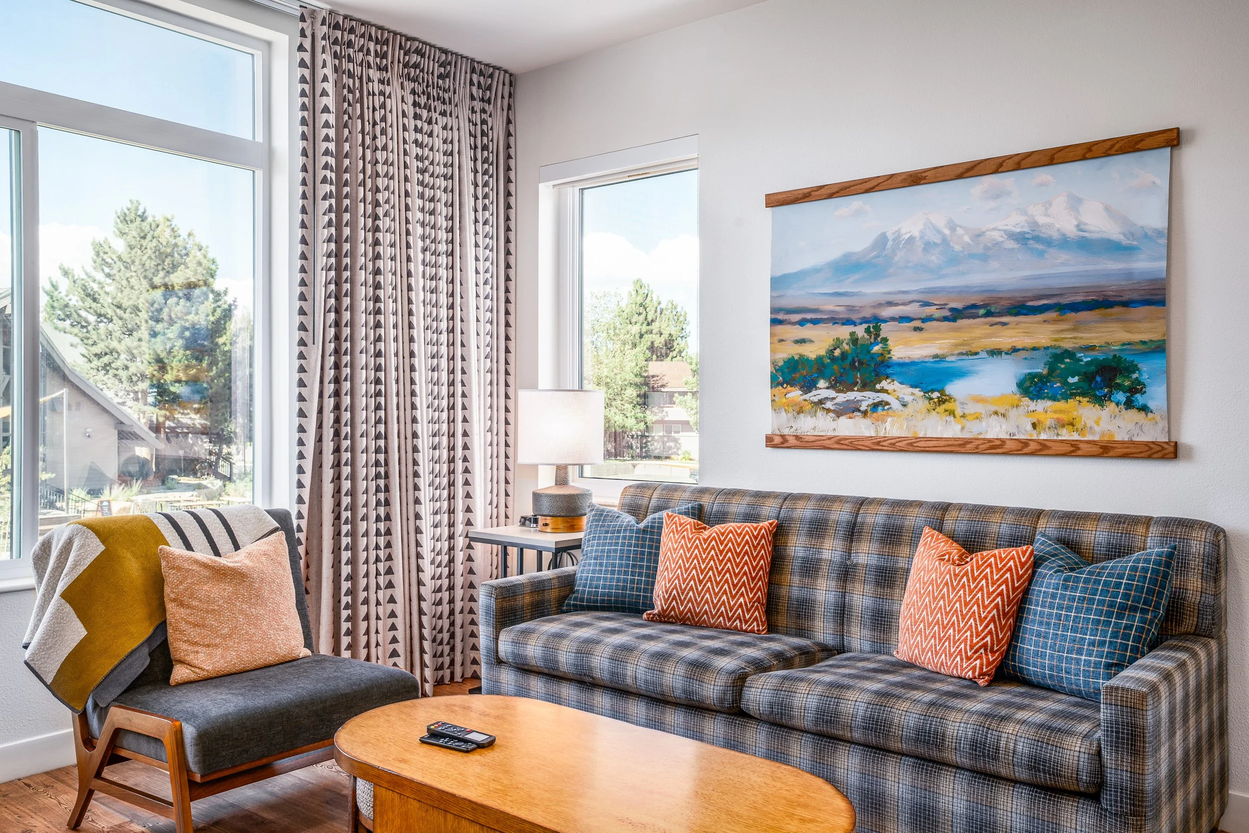 Condo living room with plaid sofa and mountain art beside tall windows with patterned drapes