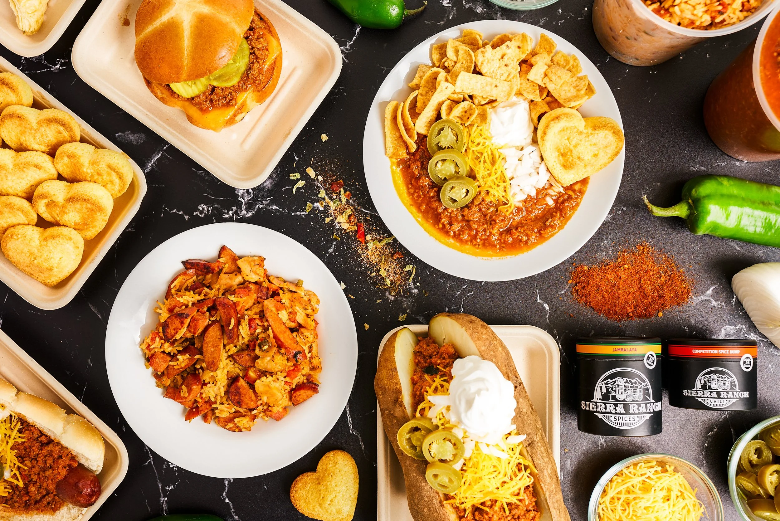 Overhead flatlay of Sierra Ranch Chili Spices brand spread including loaded chili, jambalaya, chili dog, and sliders on black marble — food brand photography by BK Captured